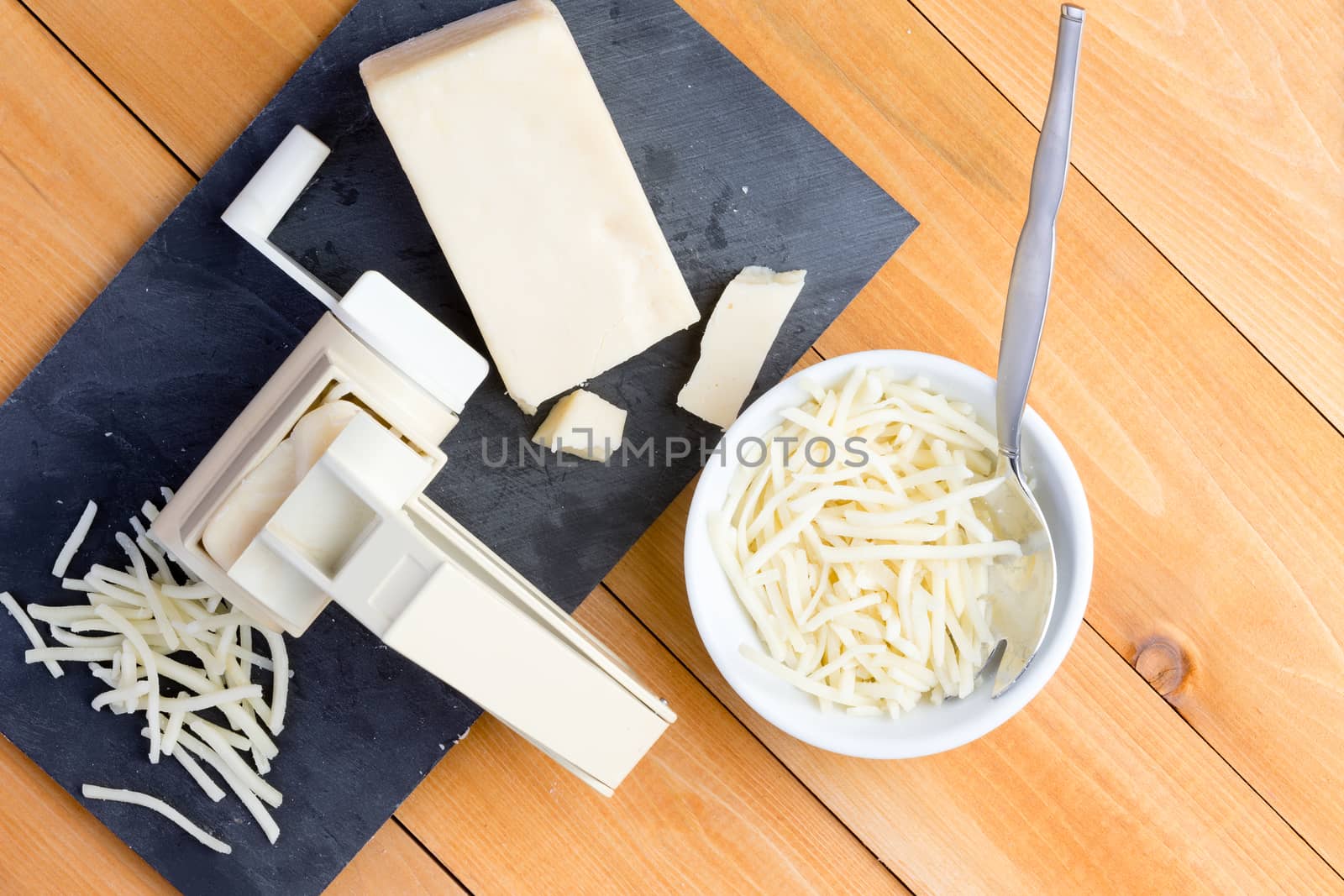 Preparing grated gruyere cheese for cooking with an overhead view of a rotary grater and wedge of cheese on a board alongside grated cheese in a bowl