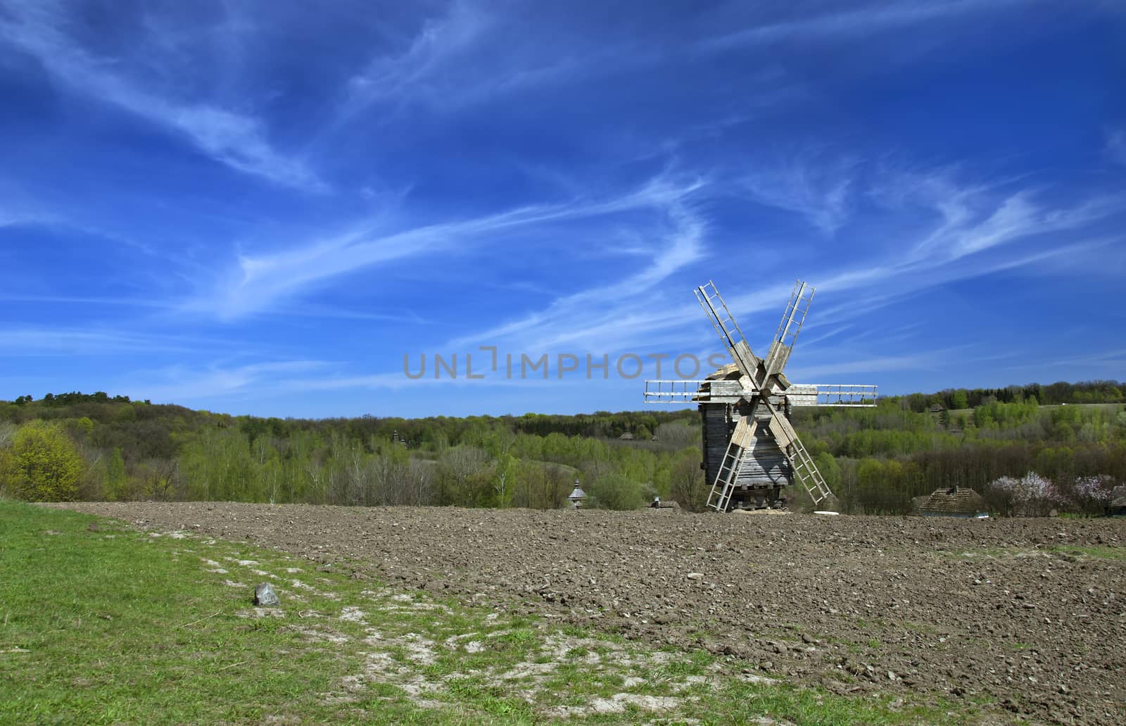 Spring landscape with a windmill in a plowed field with a blue sky and clouds on a sunny day. Ukraine.