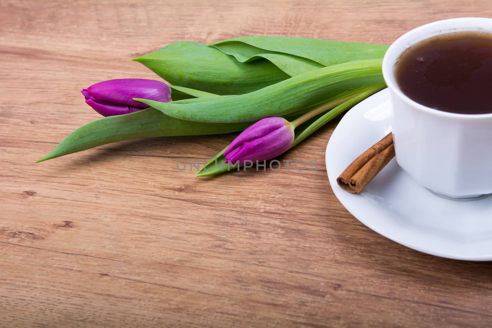 A cup of tea with cinnamon and purple tulips on a wooden background