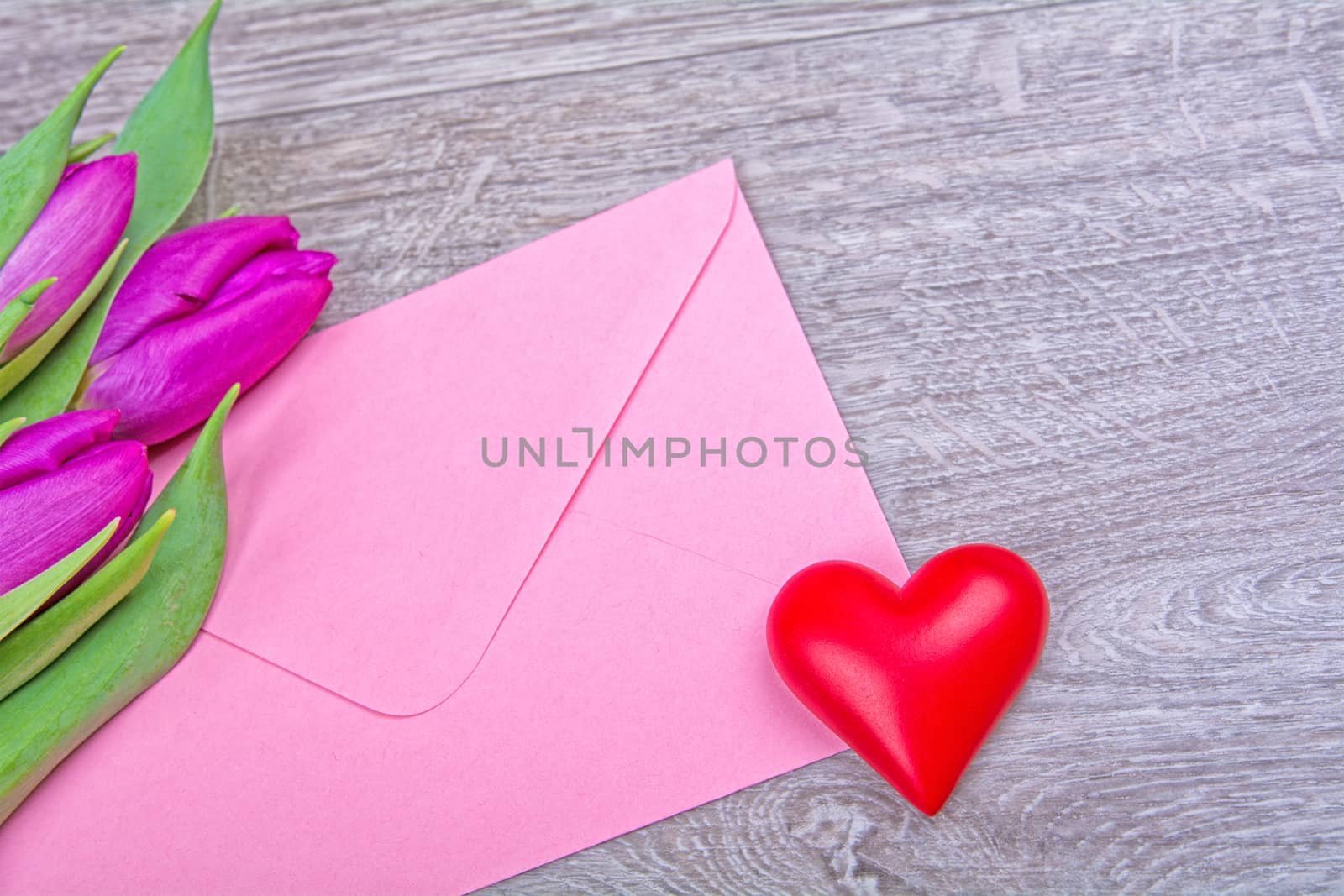 Pink envelope with red heart and purple tulips on a wooden background