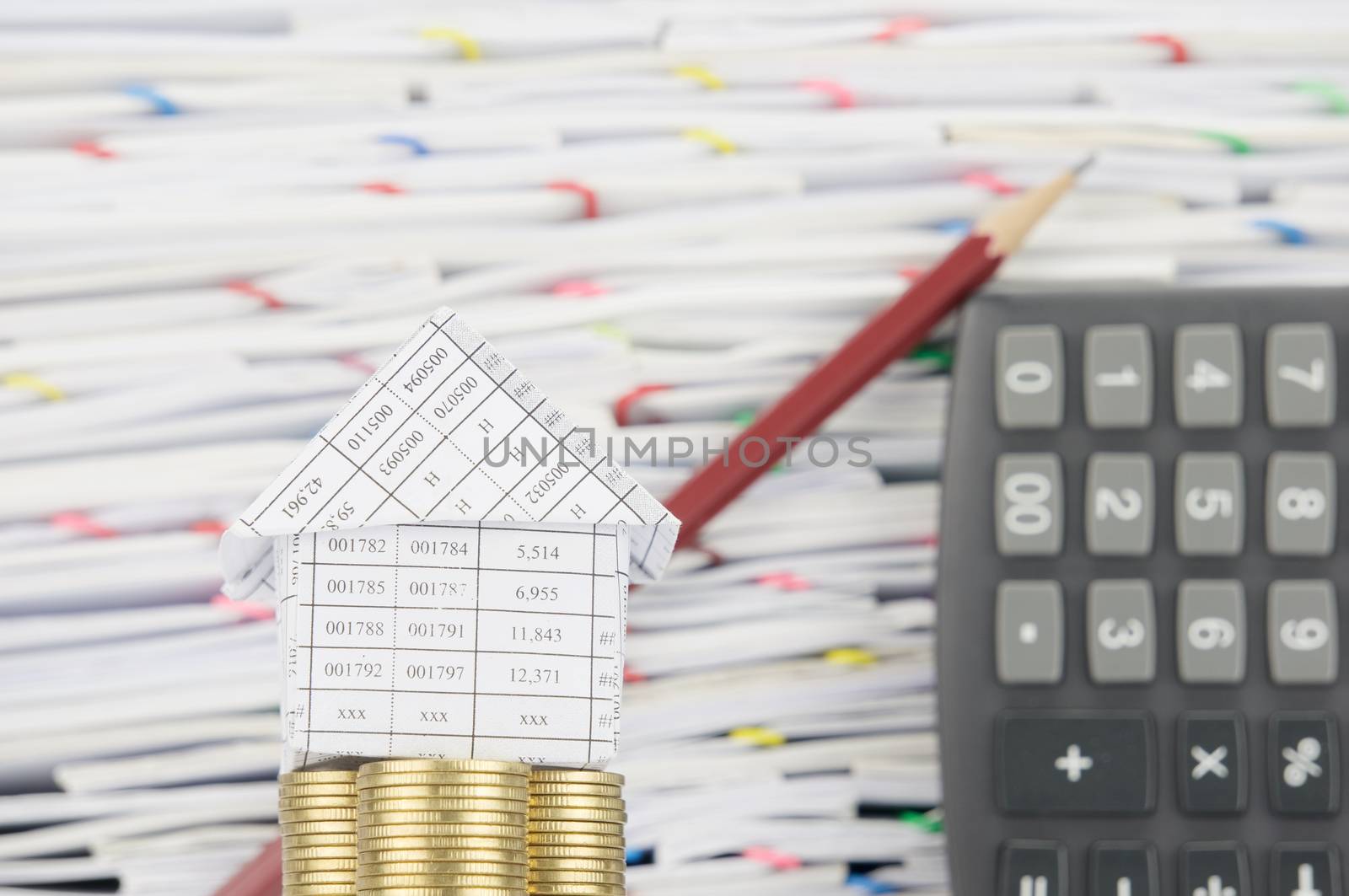 House on pile of gold coins have blur brown pencil lean calculator place vertical and overload of confused paperwork with colorful paperclip as background.