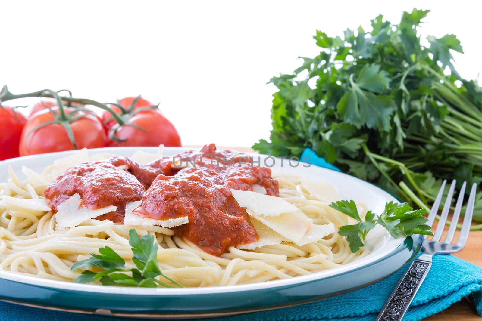 Prepared plate of spaghetti pasta garnished with grana padano cheese, italian parsley and red sauce surrounded by tomatoes and fork on napkin