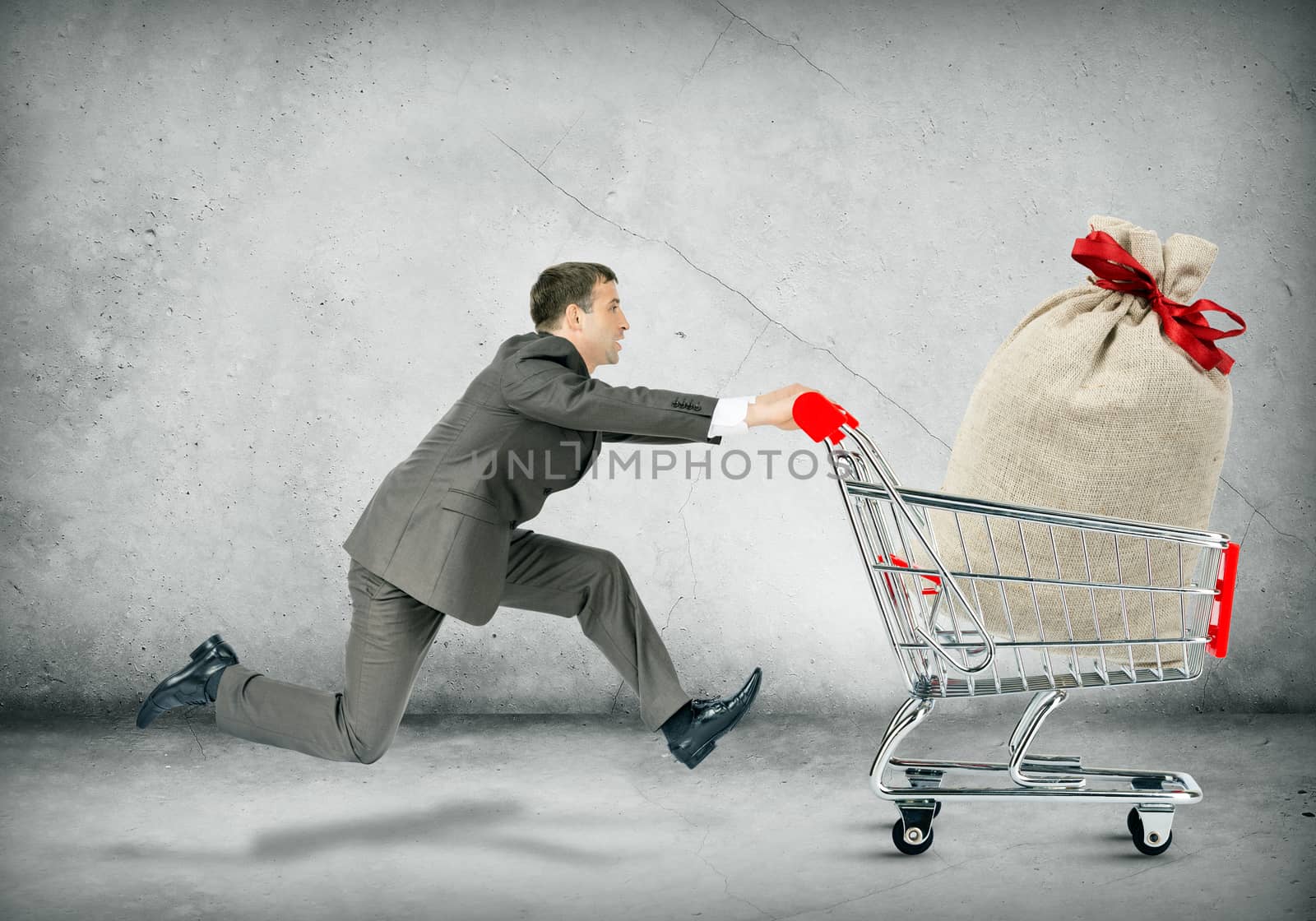 Businessman pushing shopping cart with money bag on grey background