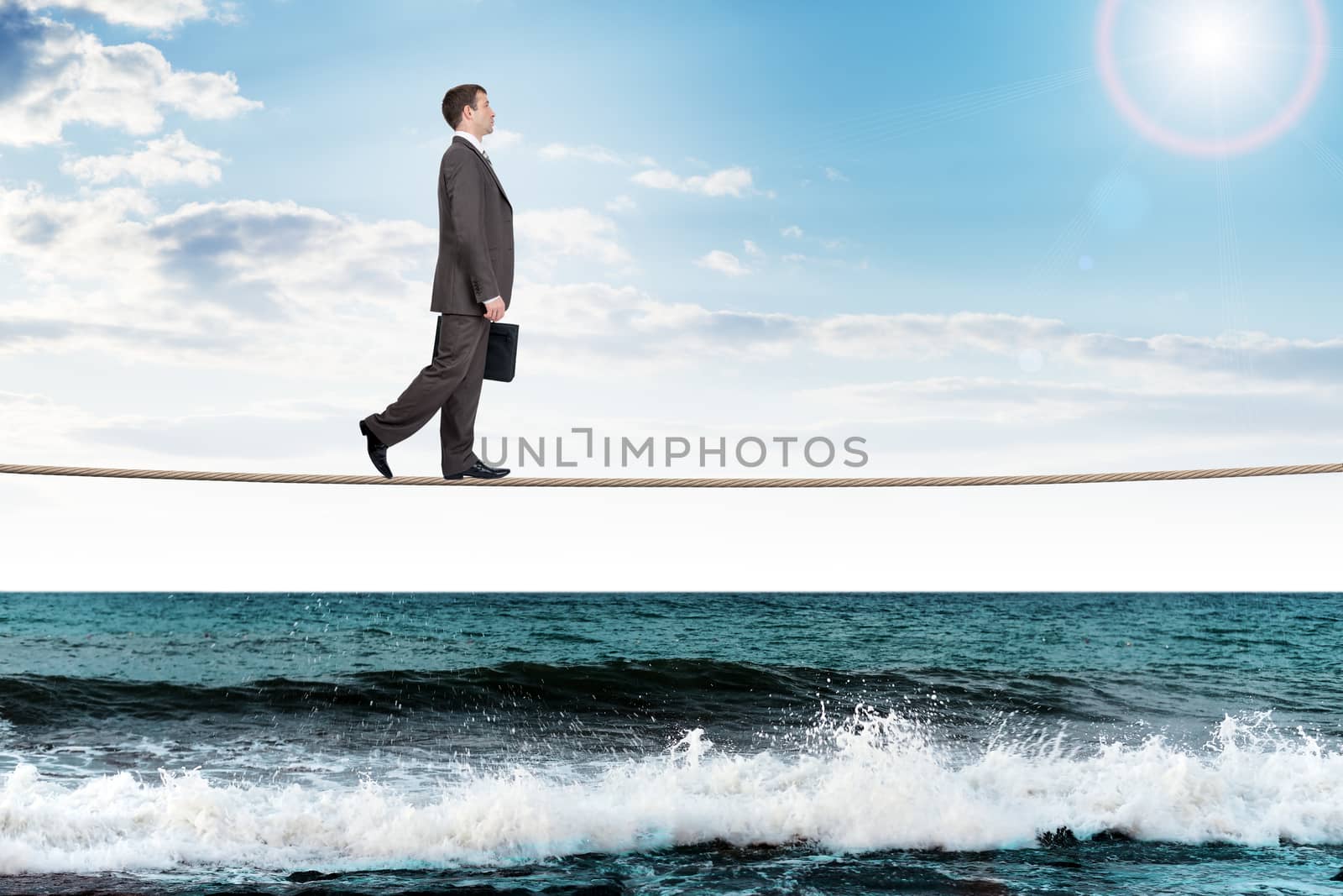Businessman with suitcase walking on rope, danger concept