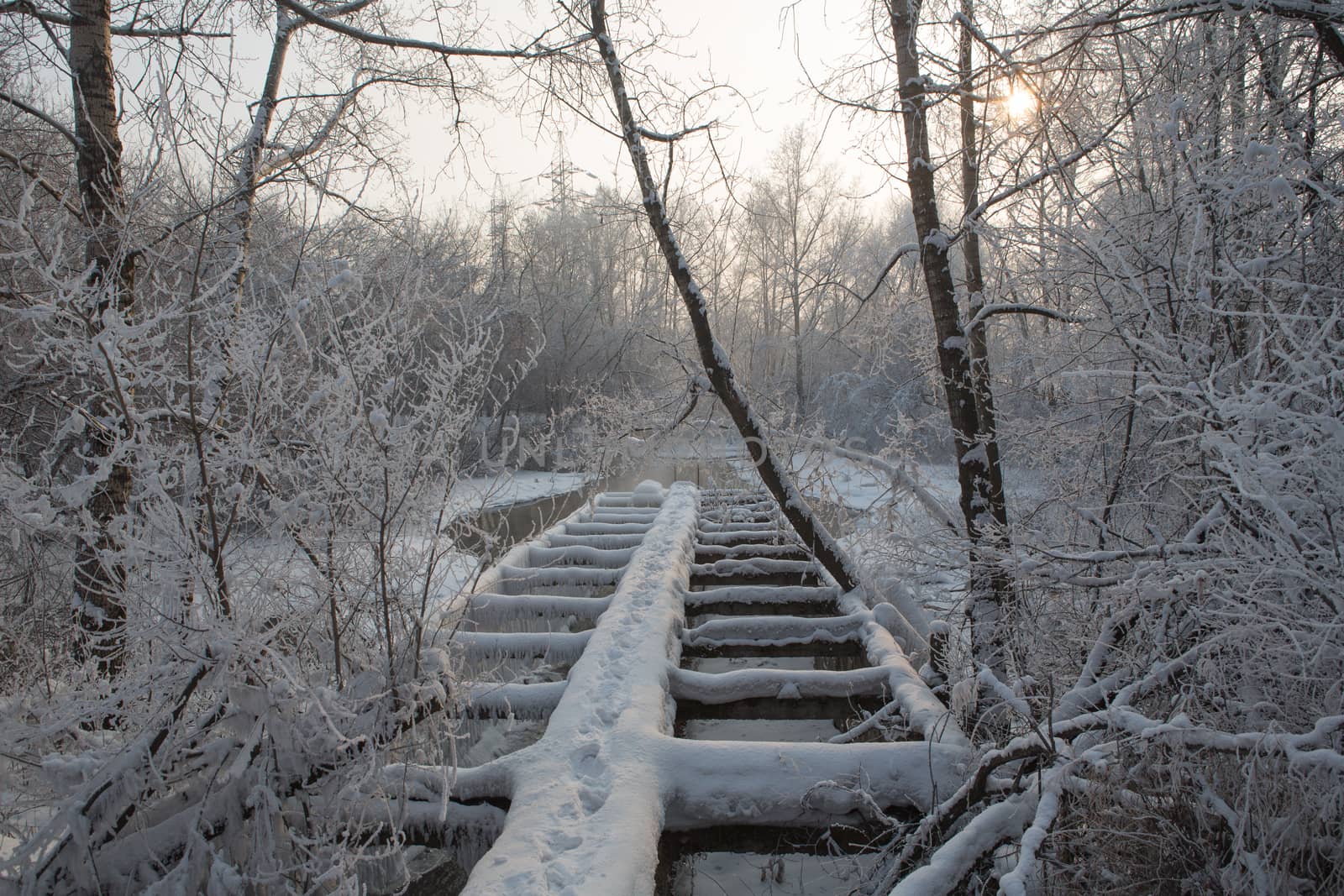 Old broken wooden pedestrian bridge covered with snow in winter