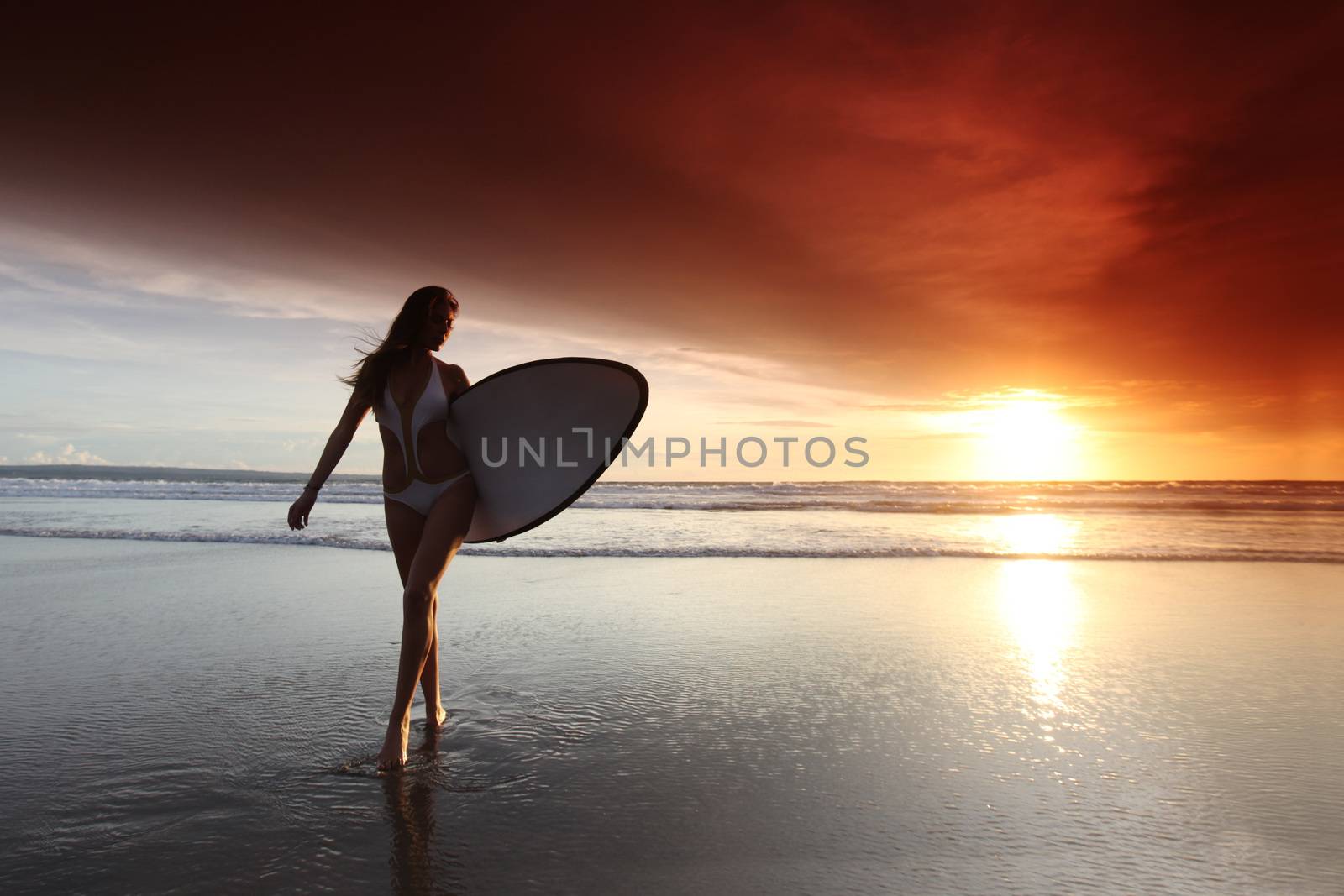 Beautiful surfer woman on the beach at sunset