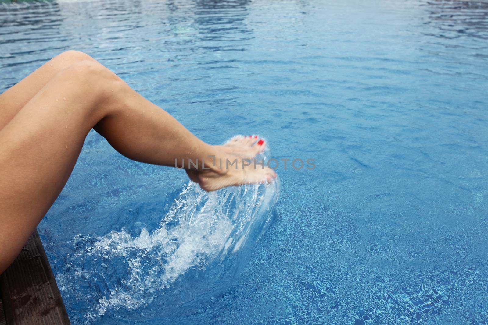 Female feet in the pool making splashes