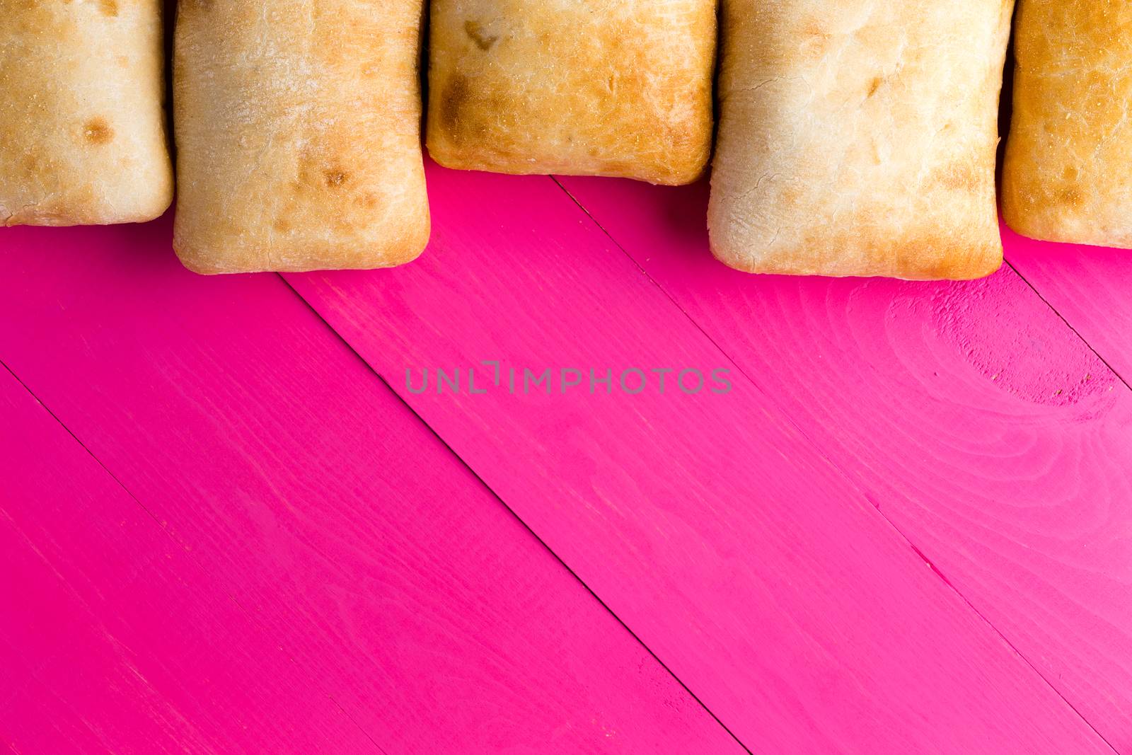 Border of Italian ciabatta bread, a crusty porous bread made with olive oil, on exotic pink wooden boards with copy space, overhead view