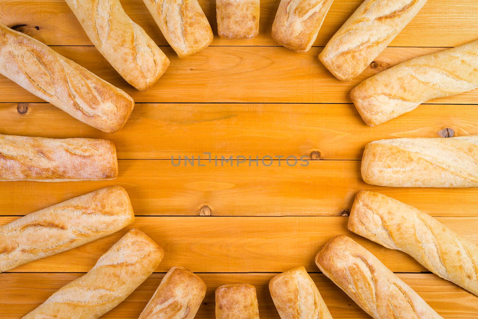 Circular frame of freshly baked crusty French bread loaves arranged in a radiating circle over a wooden table with central copy space, viewed from above
