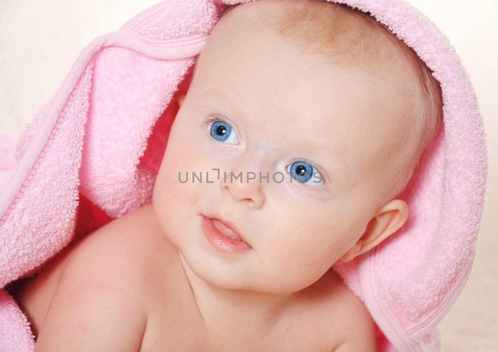 Adorable baby girl looking  under a pink towel