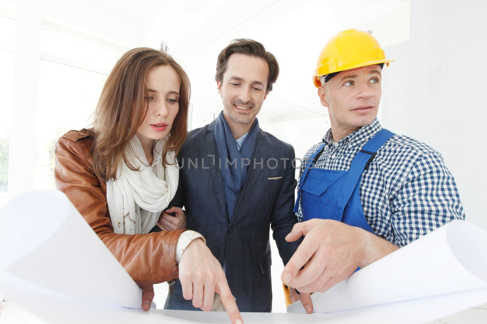 Worker shows house design plans to a young couple at construction site