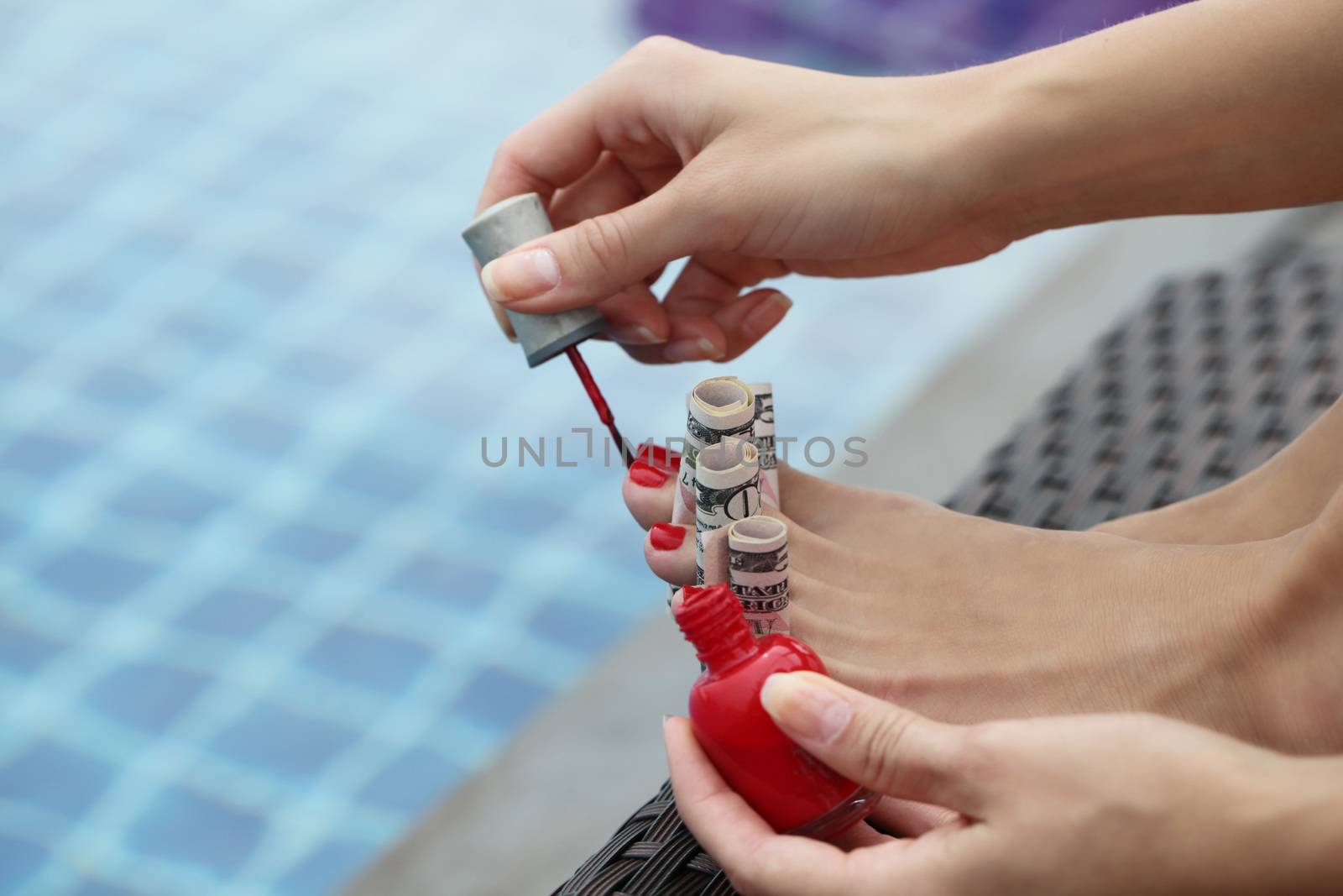 Woman painting nails using dollar bills sitting outdoors by the pool