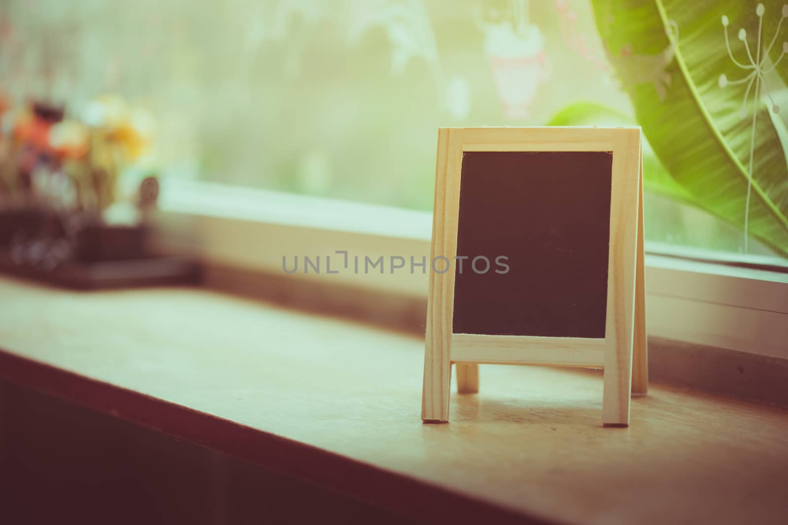 Small A-frame black board with blank area for text or message on wood bar in cafe wih vintage filter effect