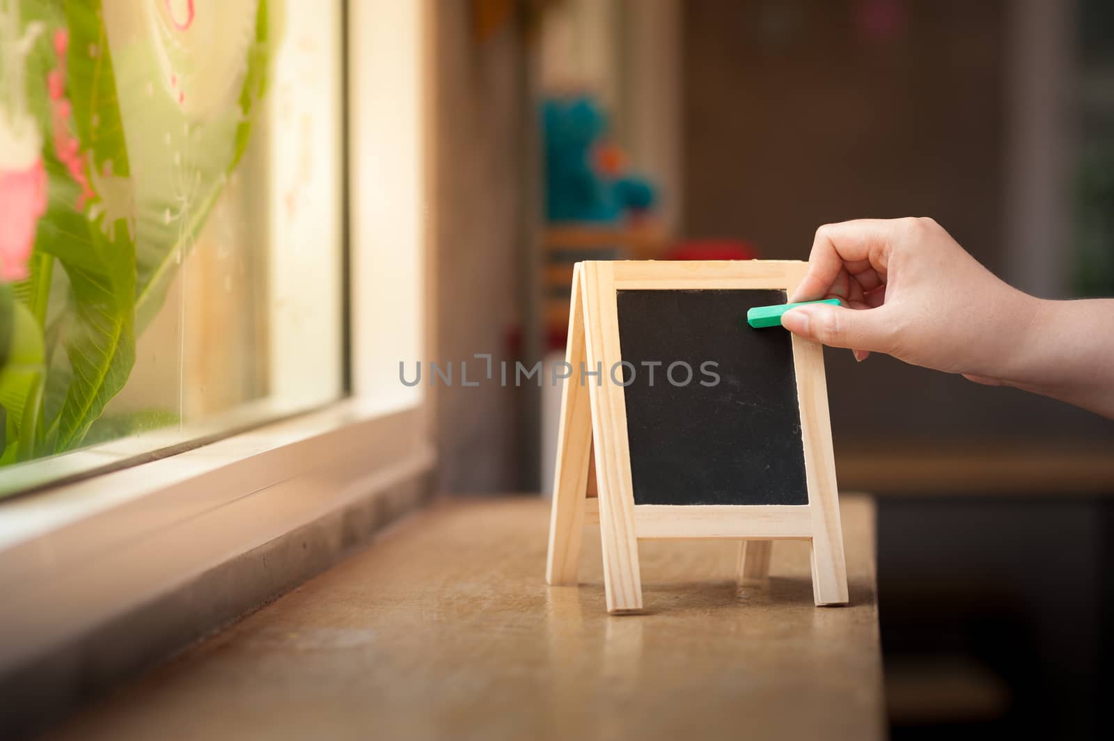 Woman right hand writing on small A-frame black board with blank area for text or message on wood bar in cafe