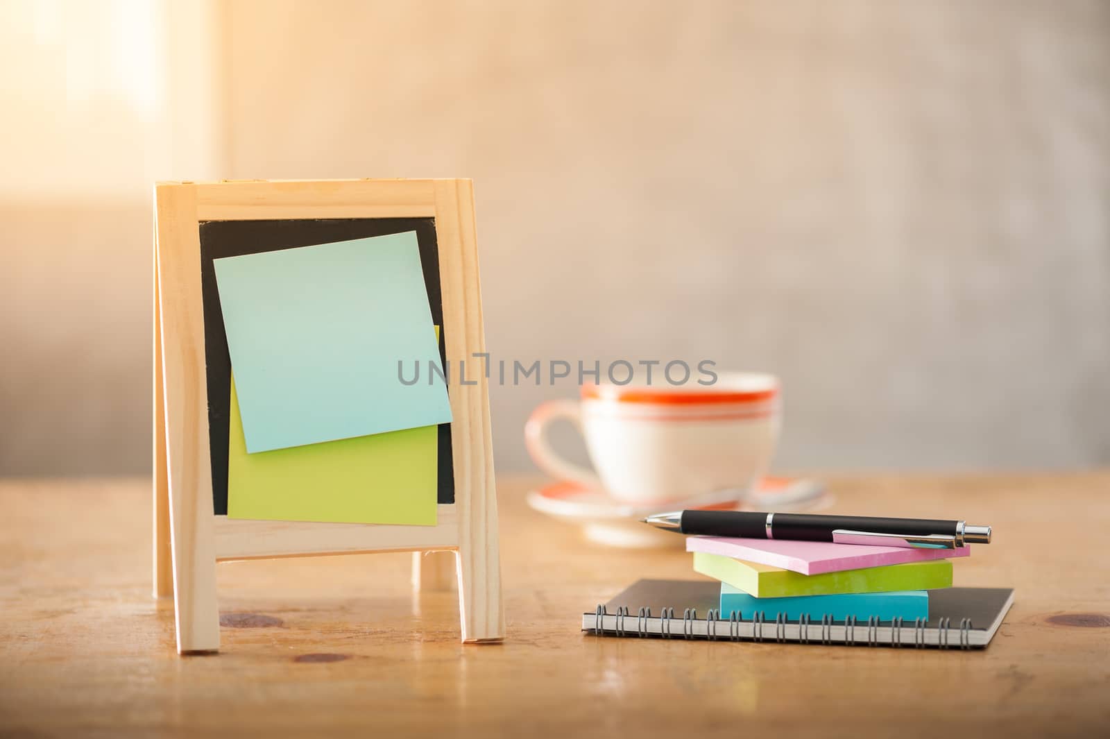 Sticky paper with blank area for text or message stick on small A-frame black board beside pen and notepad on wood table in morning time