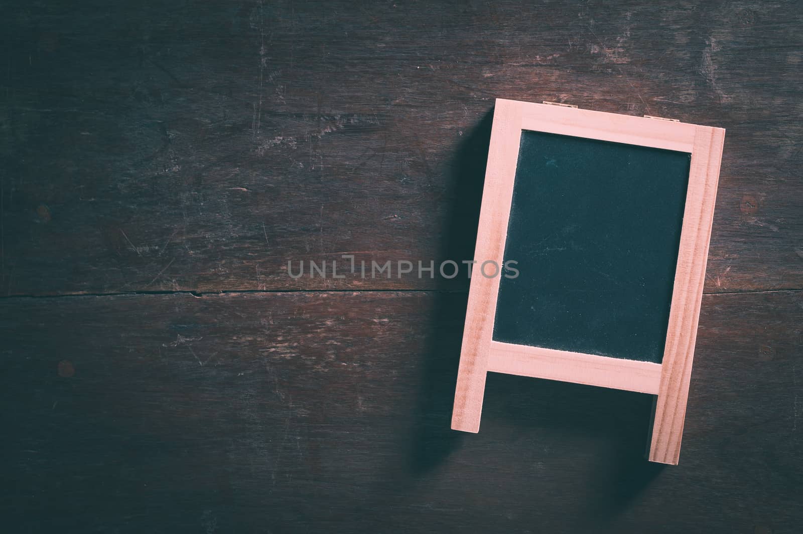 Small A-frame black board with blank area for text or message on rustic wood table with low key scene and vintage filter effect