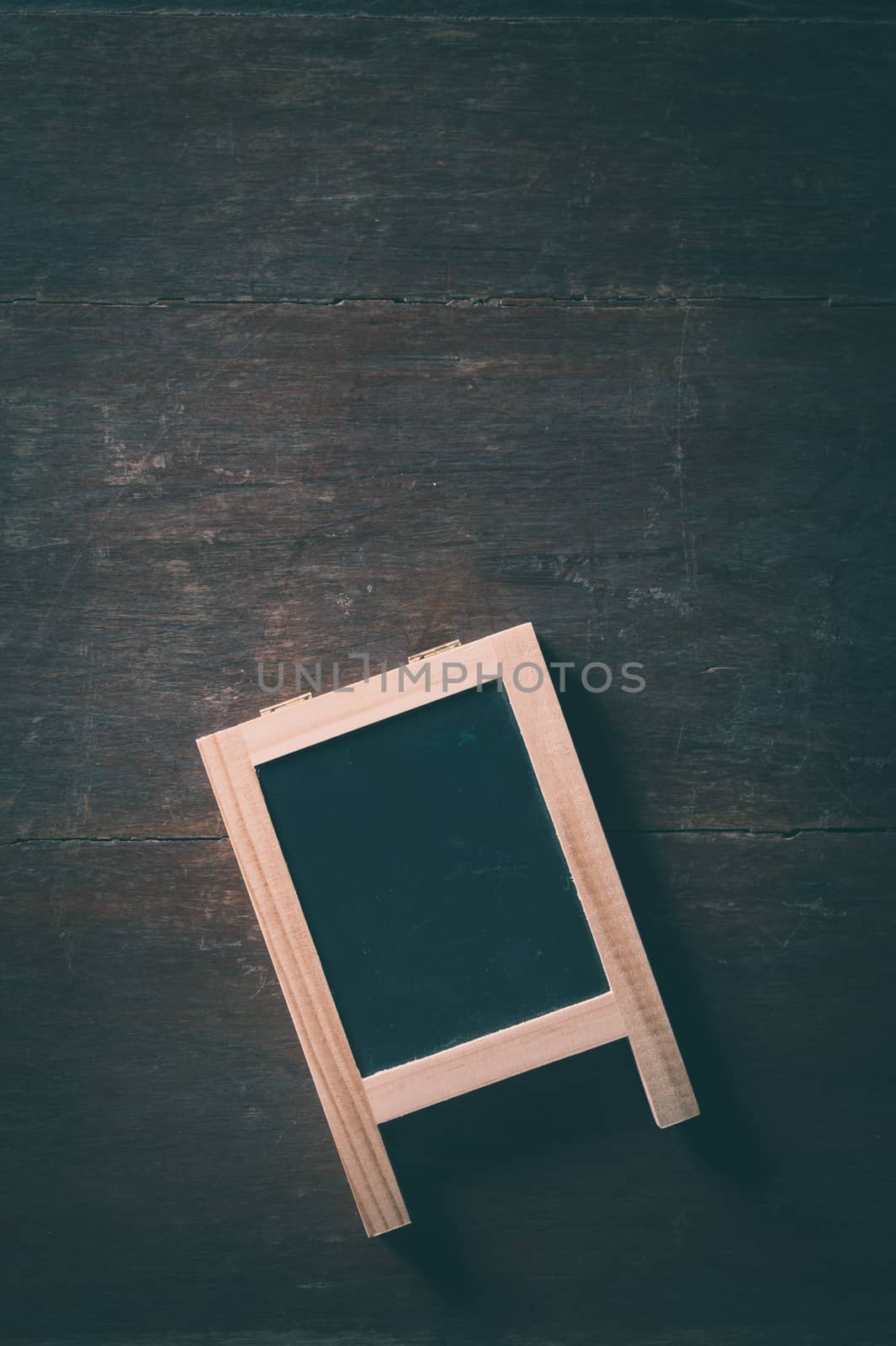 Small A-frame black board with blank area for text or message on rustic wood table with low key scene and vintage filter effect