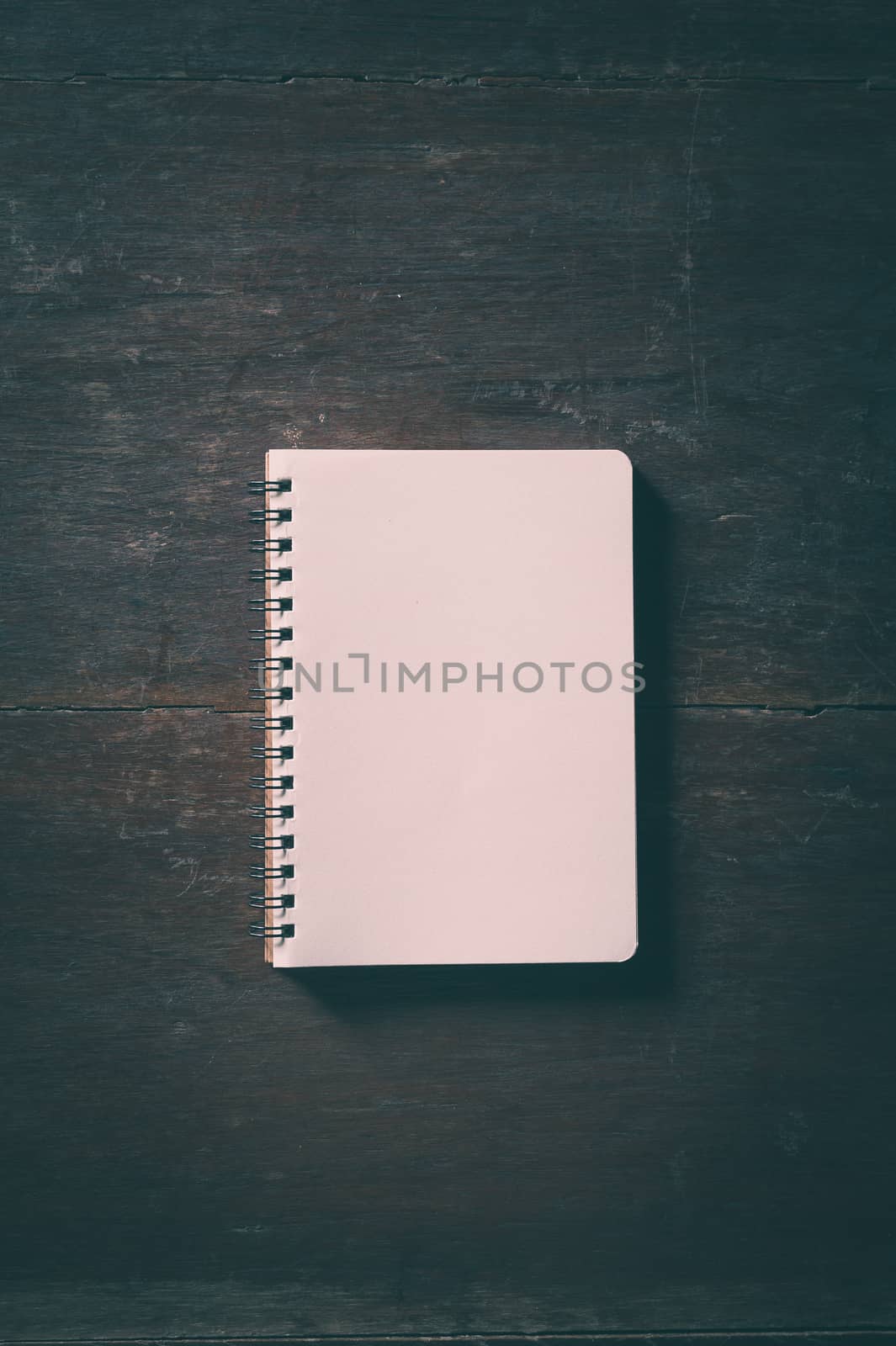 Small opened notepad with blank area for text or message and pen on rustic wood table with low key scene and vinatage filter effect