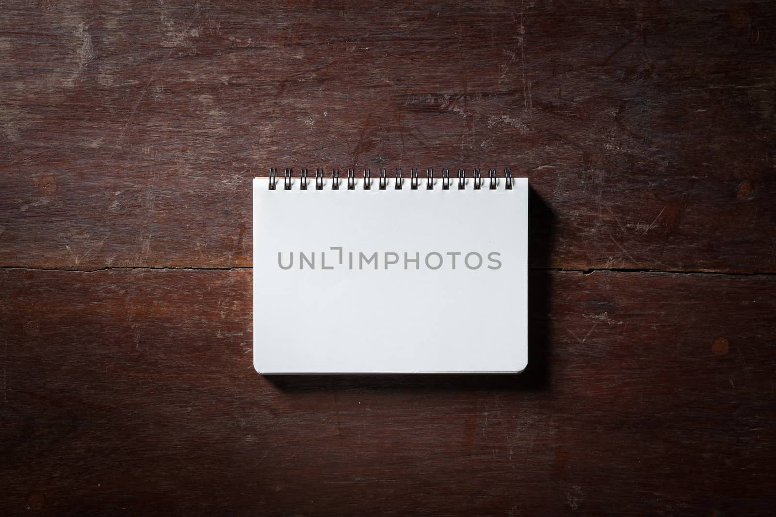 Small opened notepad with blank area for text or message and pen on rustic wood table with low key scene.
