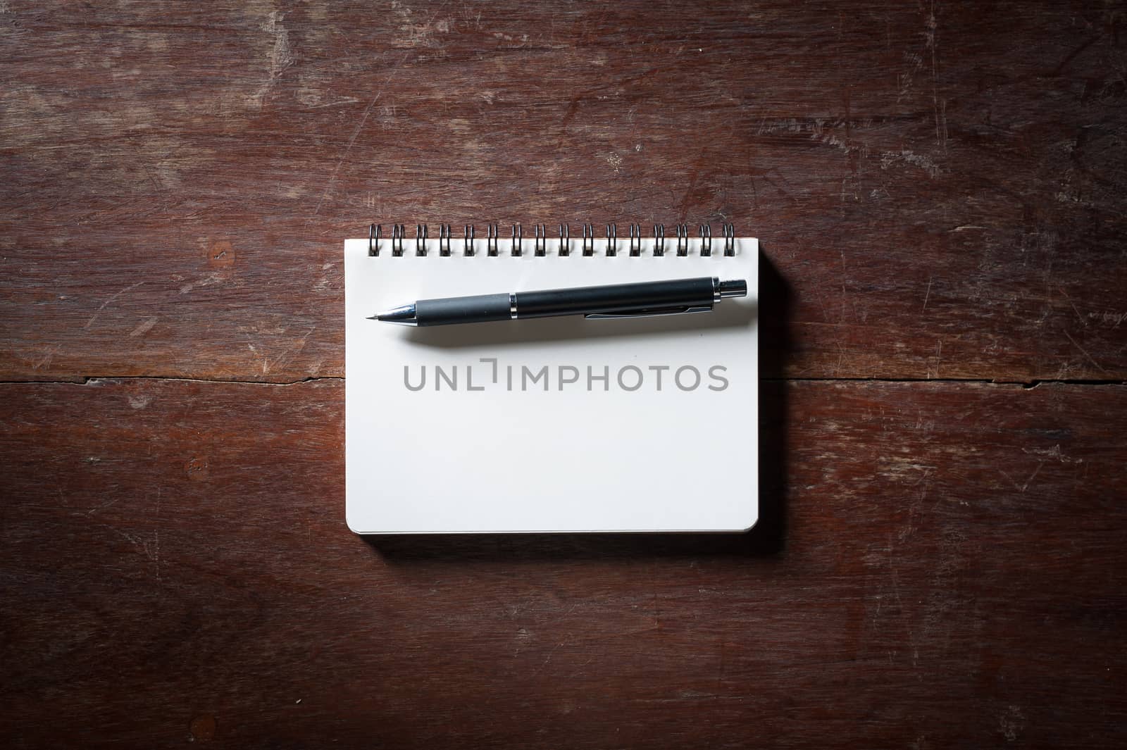 Small opened notepad with blank area for text or message and pen on rustic wood table with low key scene.