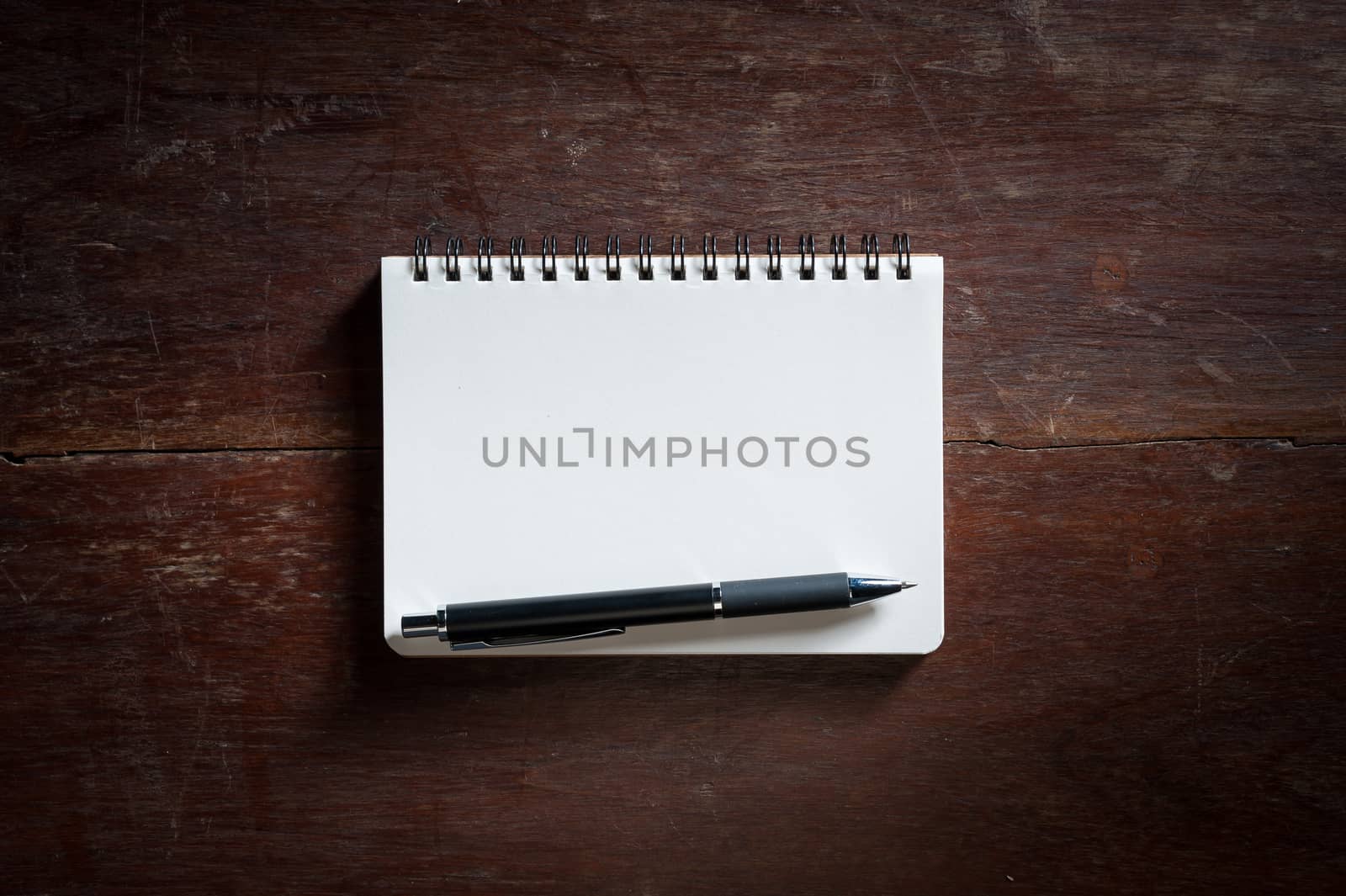 Small opened notepad with blank area for text or message and pen on rustic wood table with low key scene.