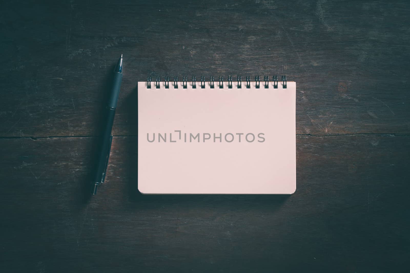 Small opened notepad with blank area for text or message and pen on rustic wood table with low key scene and vinatage filter effect