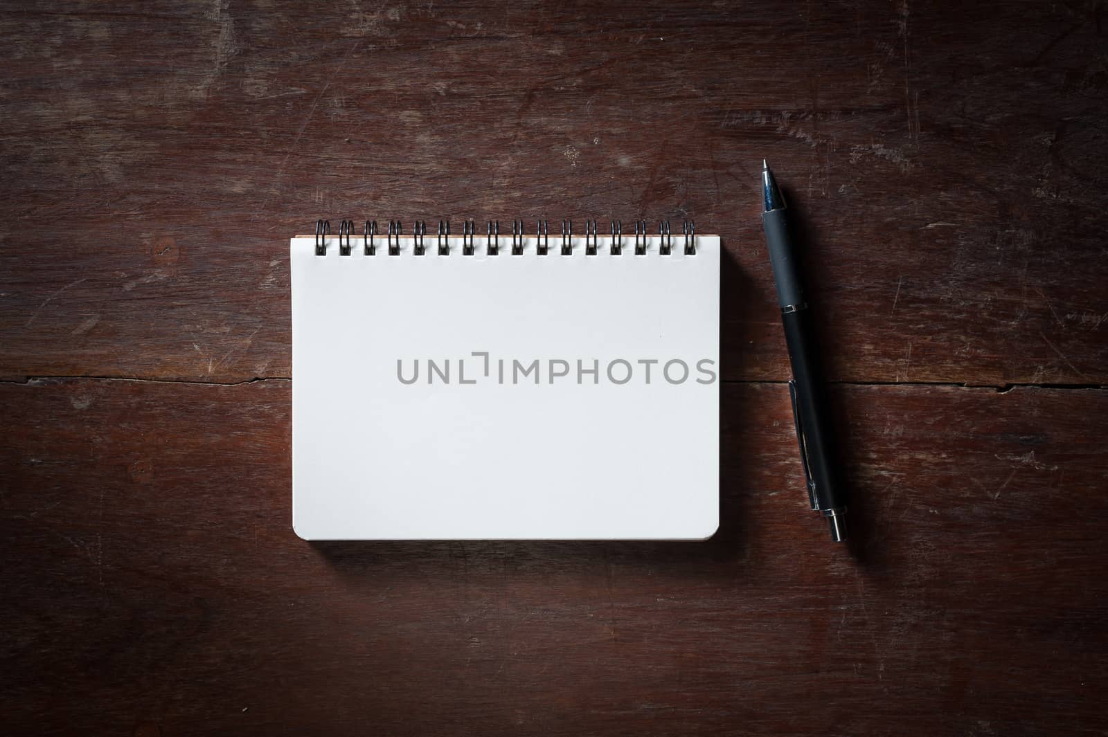 Small opened notepad with blank area for text or message and pen on rustic wood table with low key scene.