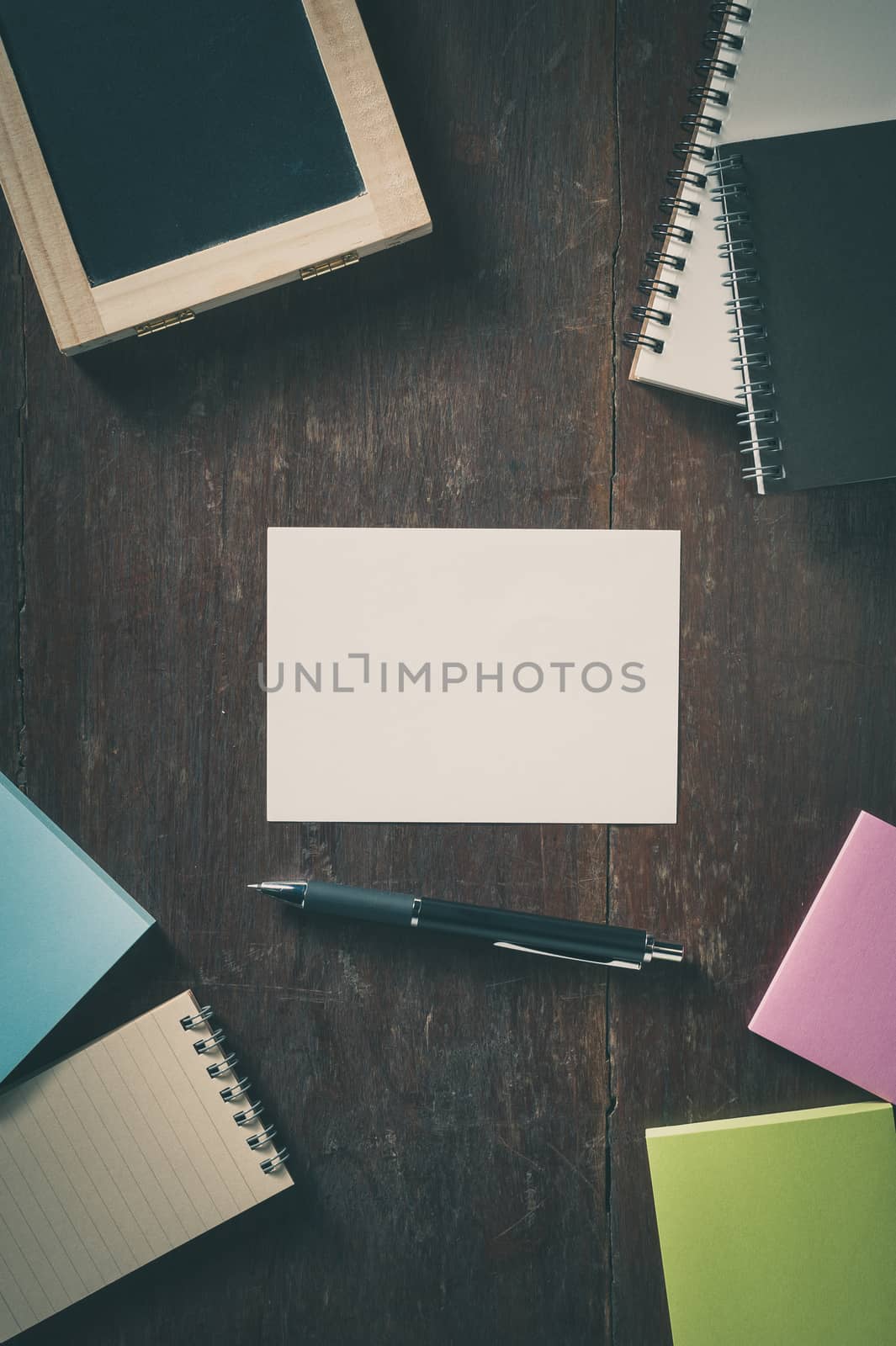 Blank paper with area for text or message, pen, notebook, and sticky paper on wood table with low key scene and vintage filter effect