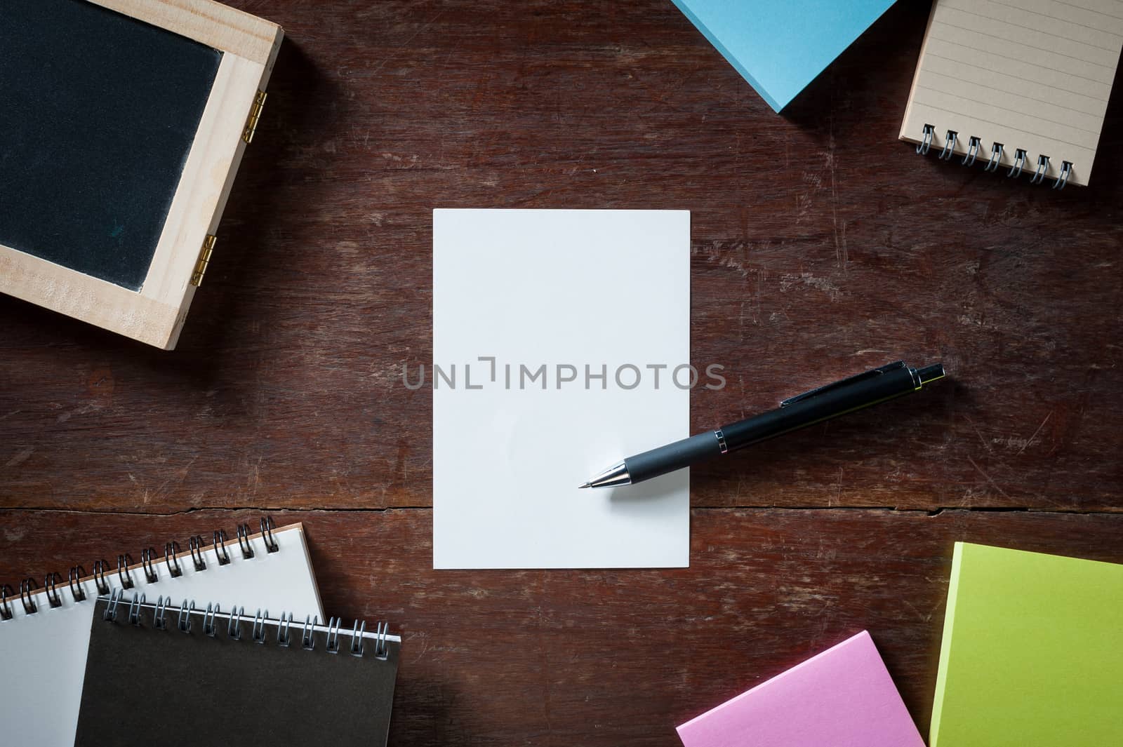 Blank paper with area for text or message, pen, notebook, and sticky paper on wood table with low key scene