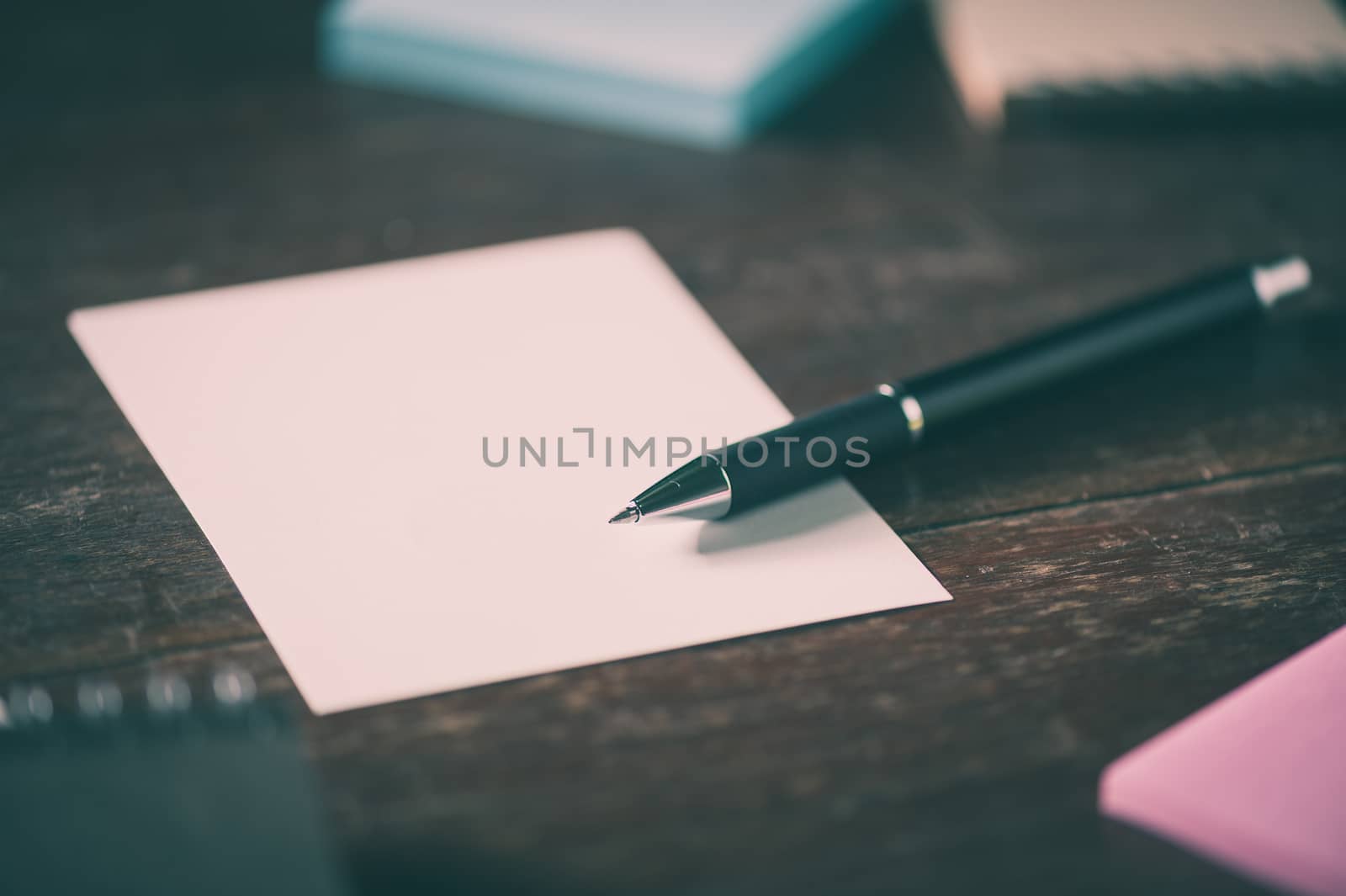 Blank paper, pen, notebook, and sticky paper on wood table with vintage filter effect