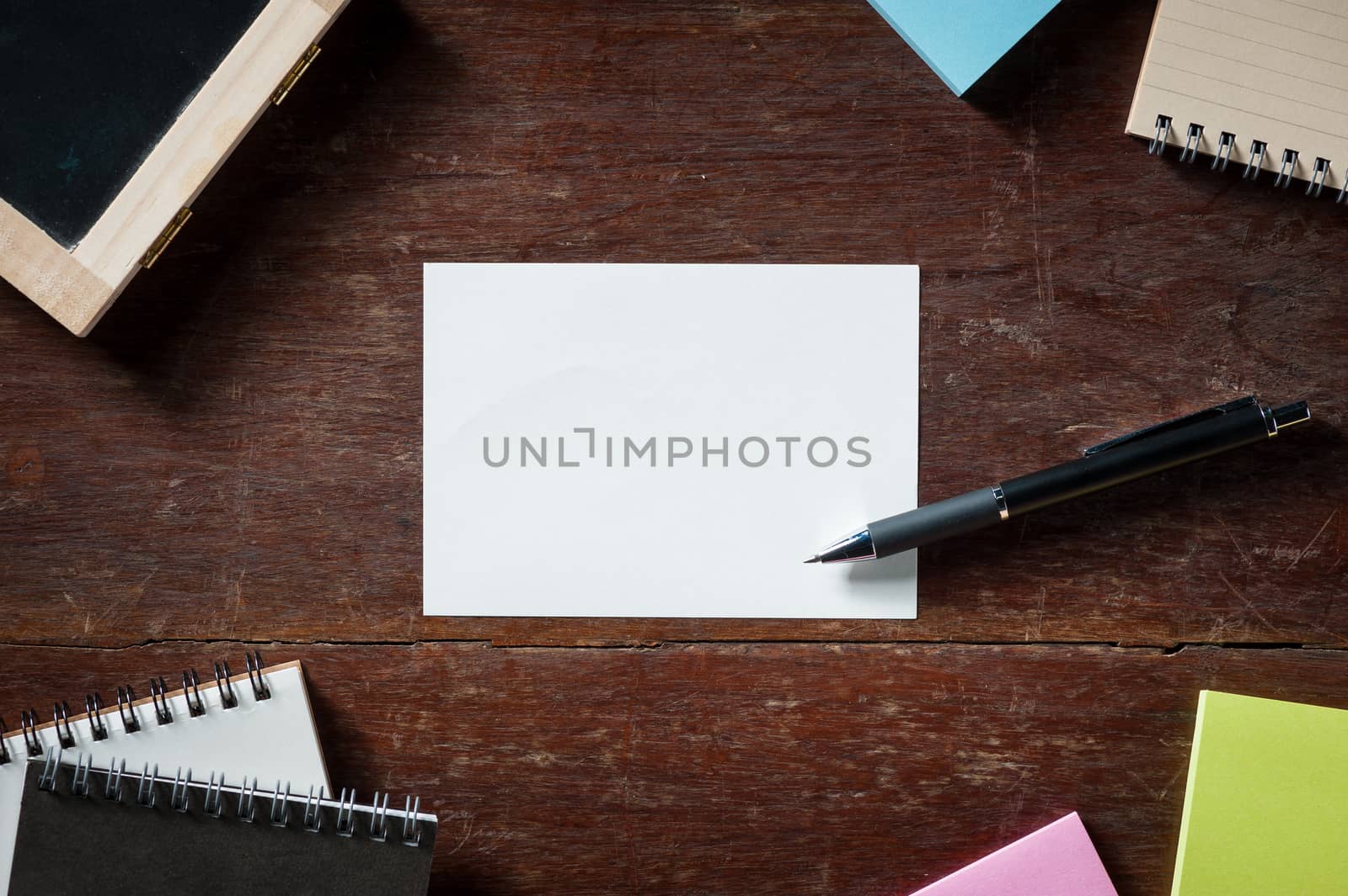 Blank paper with area for text or message, pen, notebook, and sticky paper on wood table with low key scene
