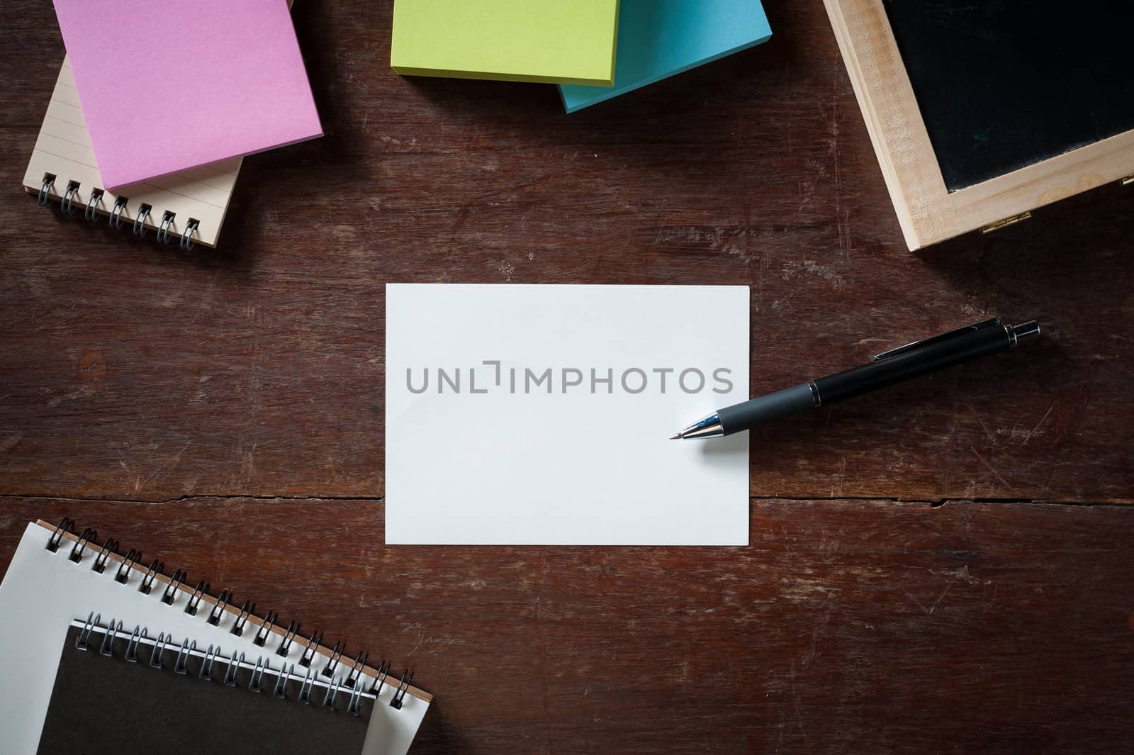Blank paper with area for text or message, pen, notebook, and sticky paper on wood table with low key scene