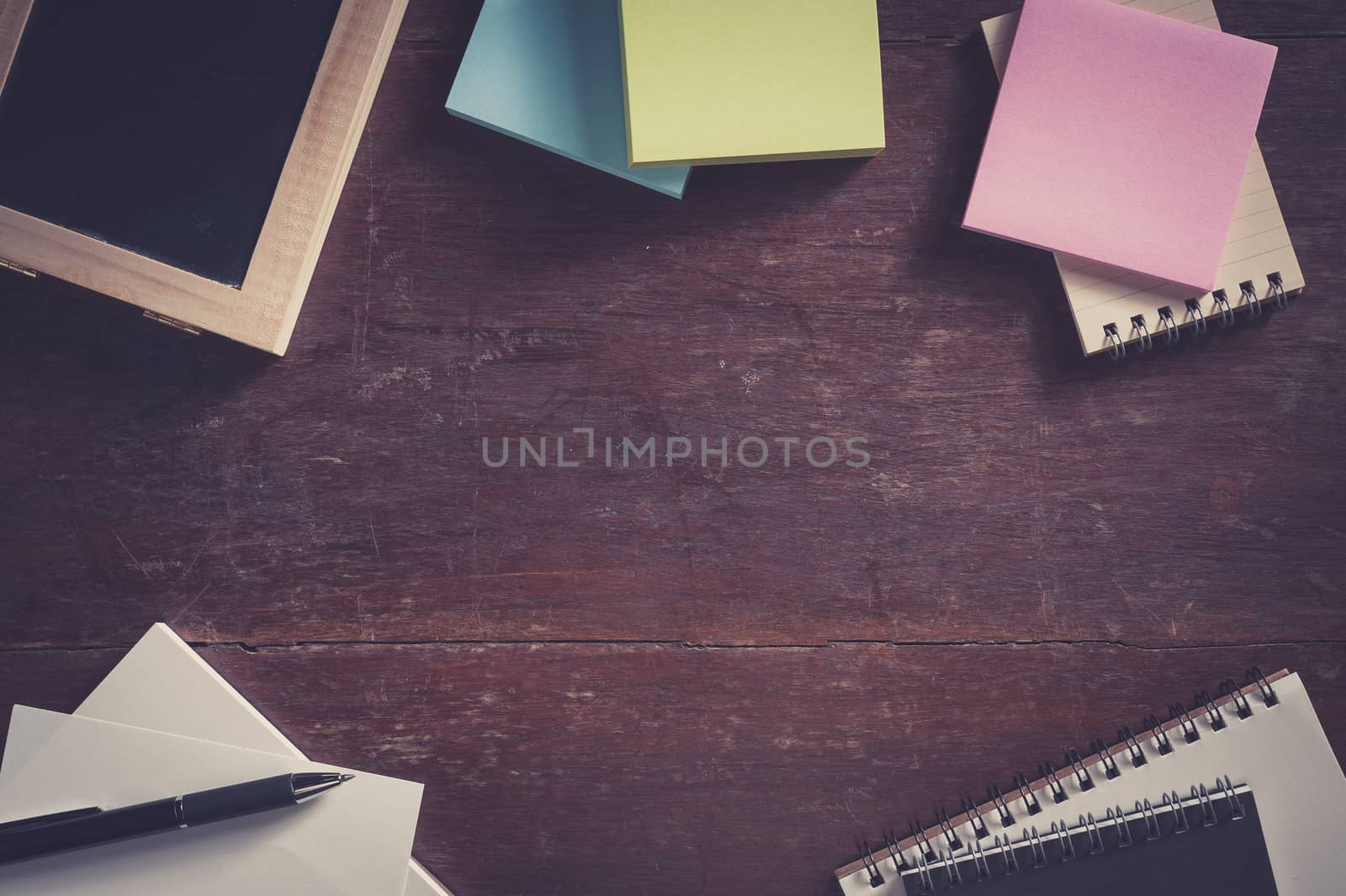 Notebooks, small black board, blank paper, sticky paper on wood table with low key scene and vintage filter effect