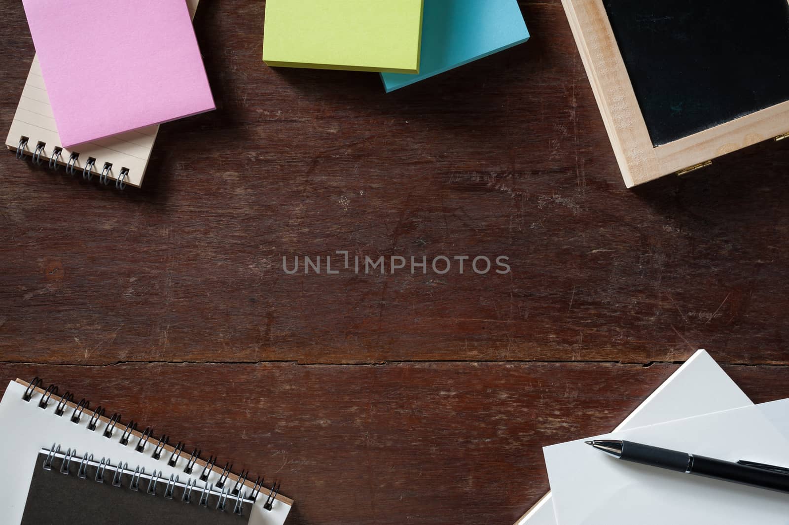 Notebooks, small black board, blank paper, sticky paper on wood table with low key scene