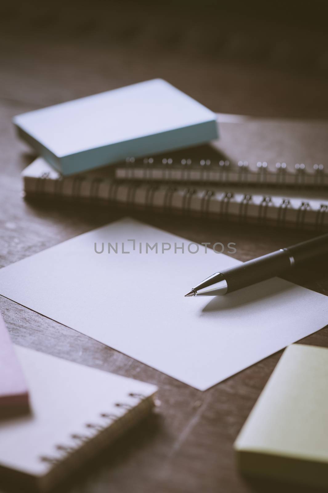 Blank paper on wood table with notebooks on wood table with low key scene and vintage filter effect