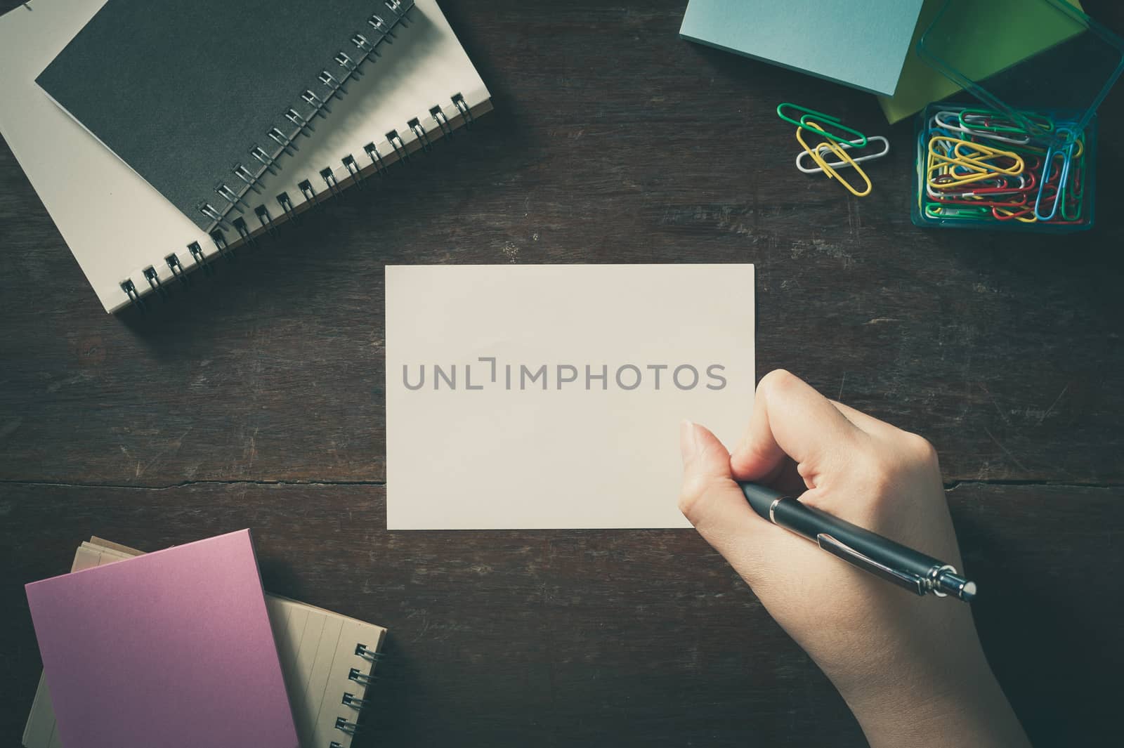 Woman right hand writing on notepad with blank area for text or message on wood table with low key scene and vintage filter effect