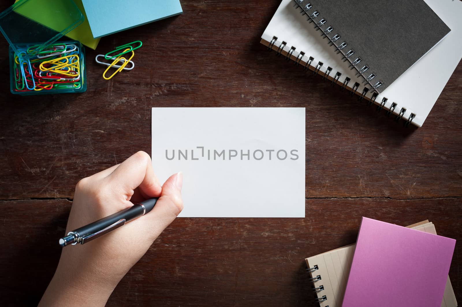 Woman left hand writing on notepad with blank area for text or message on wood table with low key scene