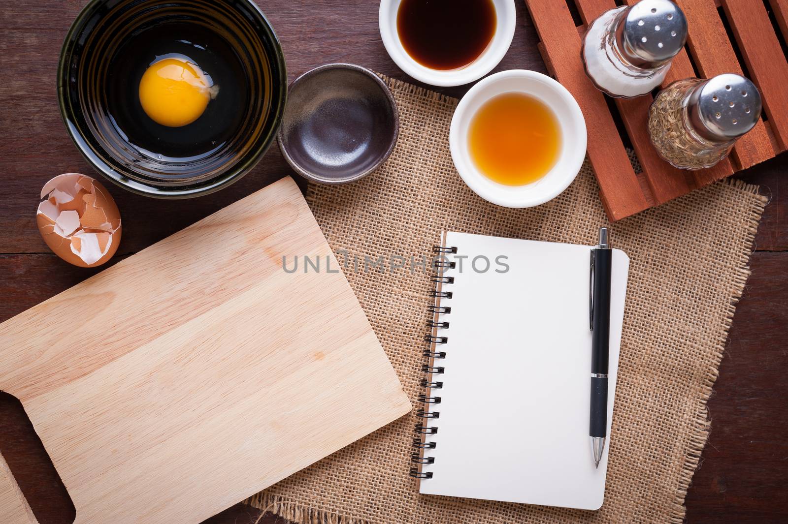 Preparation for cooking in home kitchen. Chopping board, notepad for check list, egg, and ingredients on wood table.