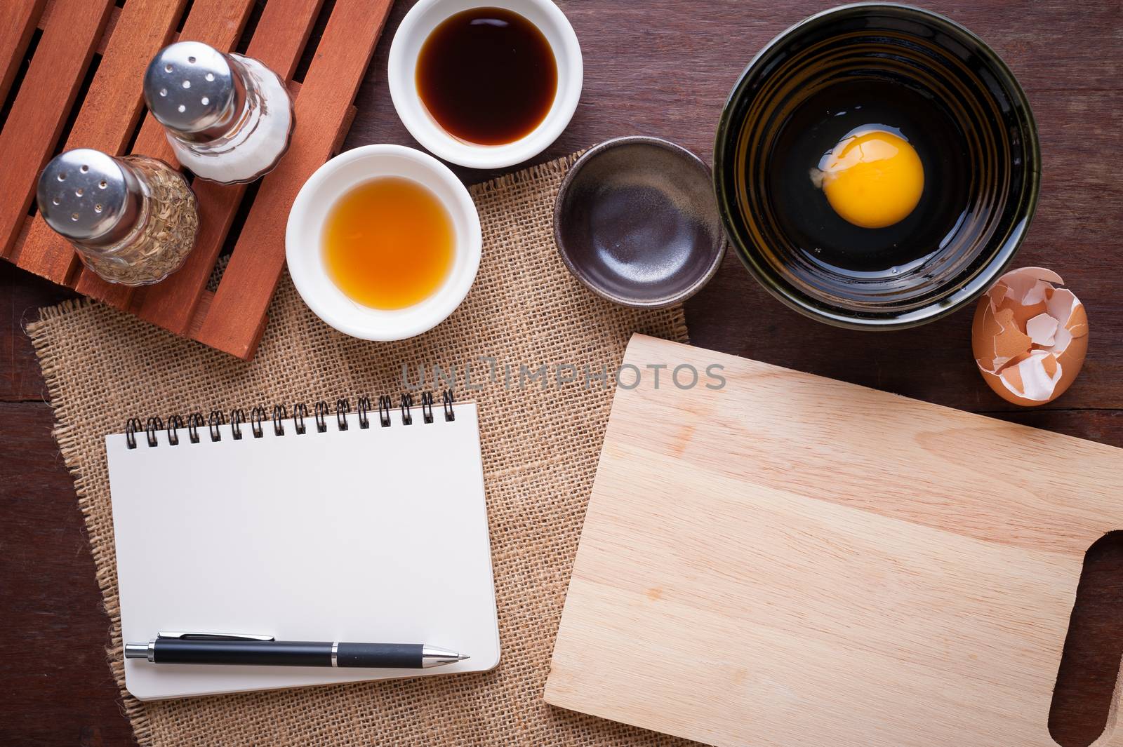 Preparation for cooking in home kitchen. Chopping board, notepad for check list, egg, and ingredients on wood table.