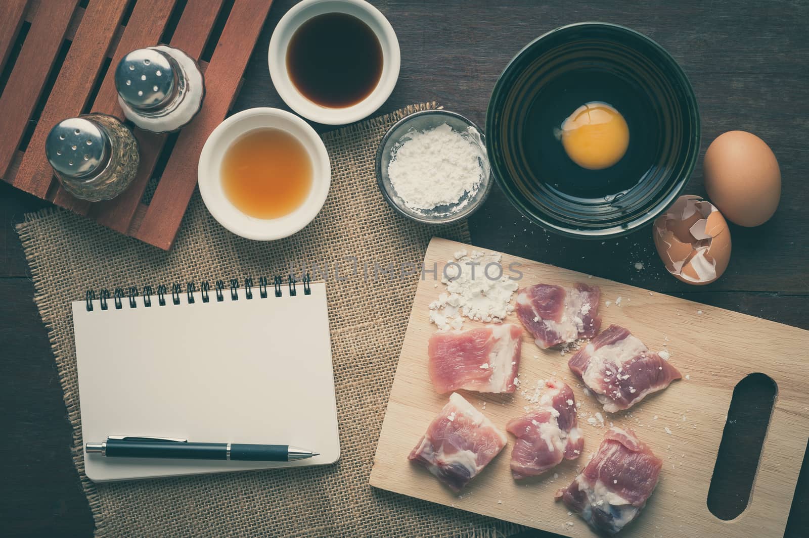 Preparation for cooking in home kitchen. Soft pork ribs on chopping board, notepad for check list, egg, and ingredients on wood table with vintage filter effect