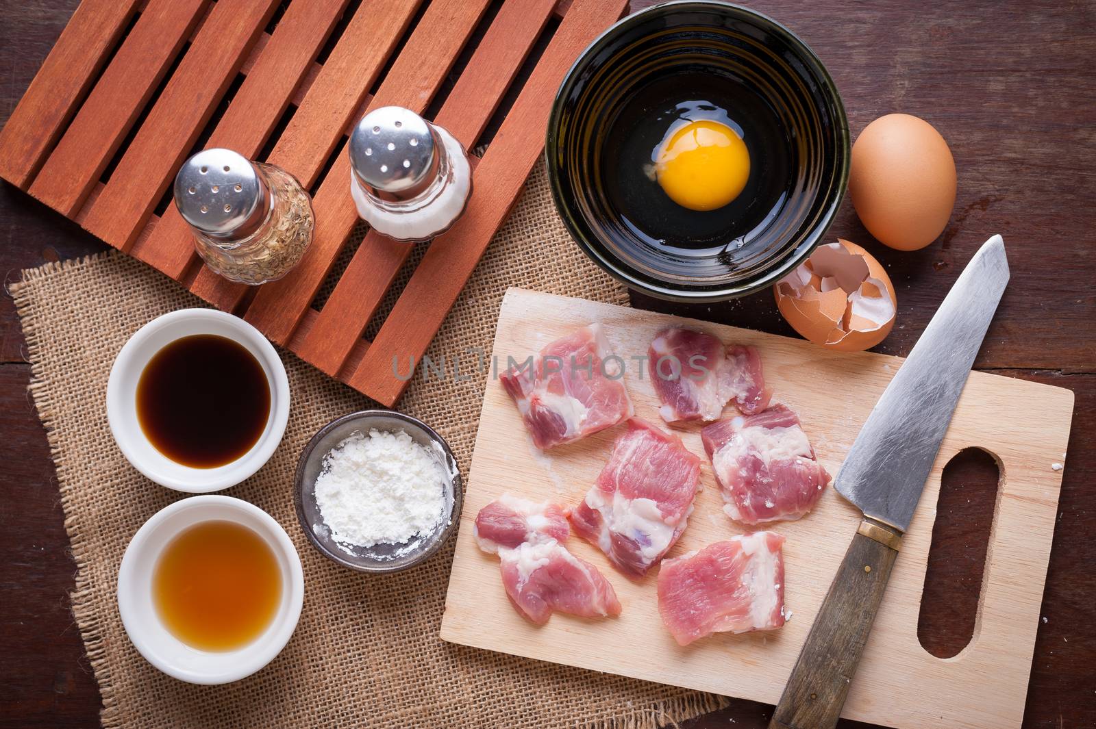 Preparation for cooking in home kitchen. Soft pork ribs on chopping board, eggs, and ingredients on wood table.