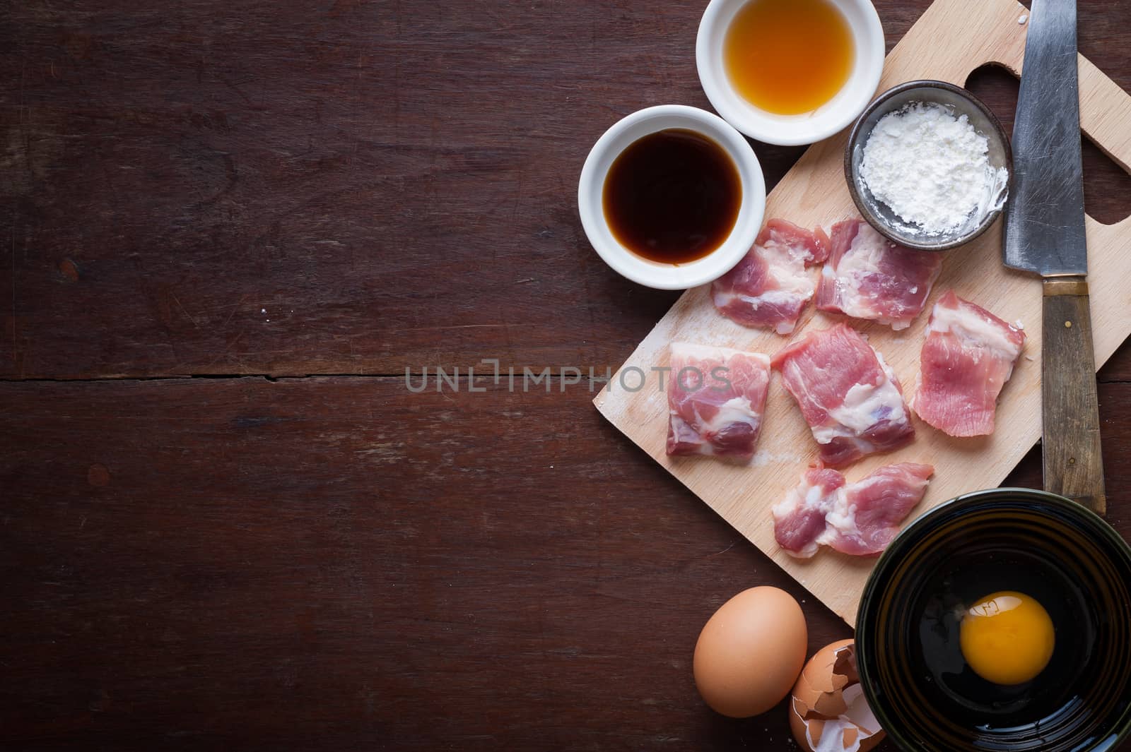 Preparation for cooking in home kitchen. Soft pork ribs on chopping board, eggs, and ingredients on wood table with low key scene in morning time