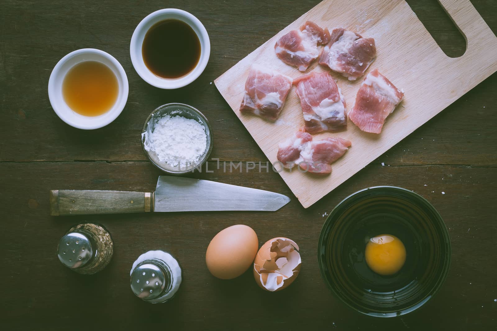 Preparation for cooking in home kitchen. Soft pork ribs on chopping board, eggs, and ingredients on wood table with vintage filter effect