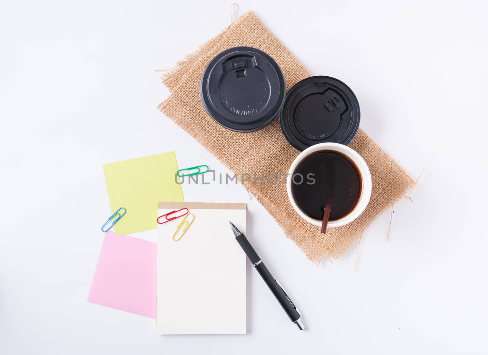Small notepad with blank space for text or message, sticky paper, pen and take away coffee cup on office table.