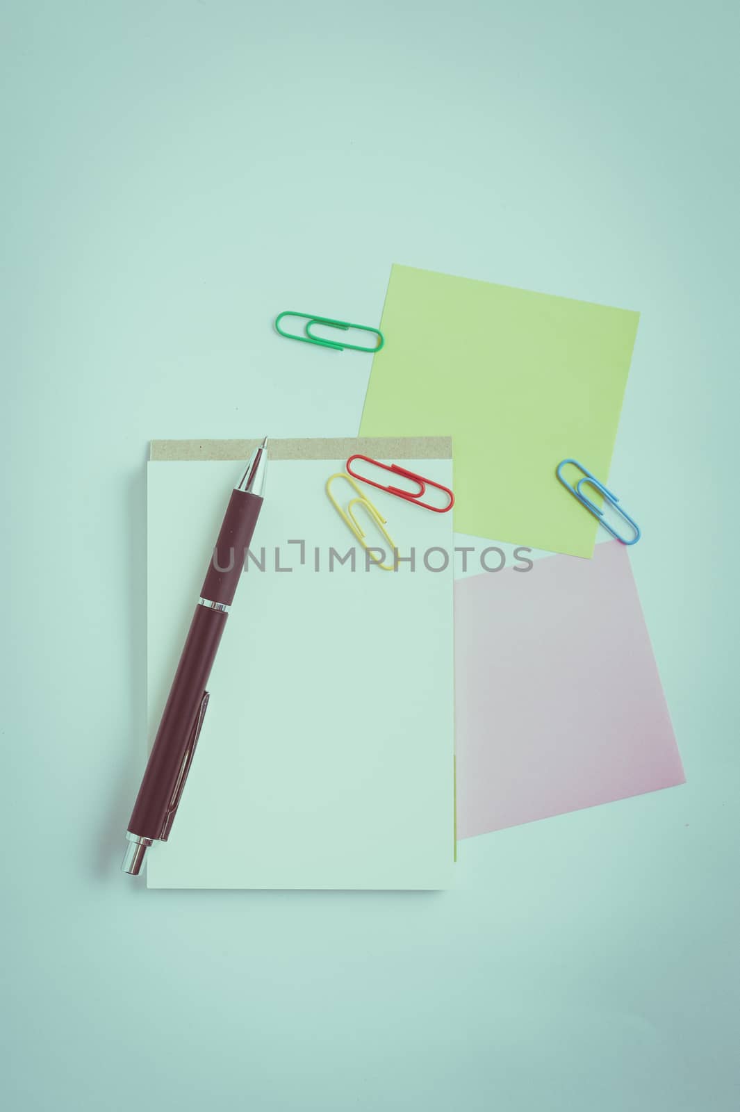 Small notepad with blank space for text or message, sticky paper, pen and paper clips on office table. with vintage filter effect
