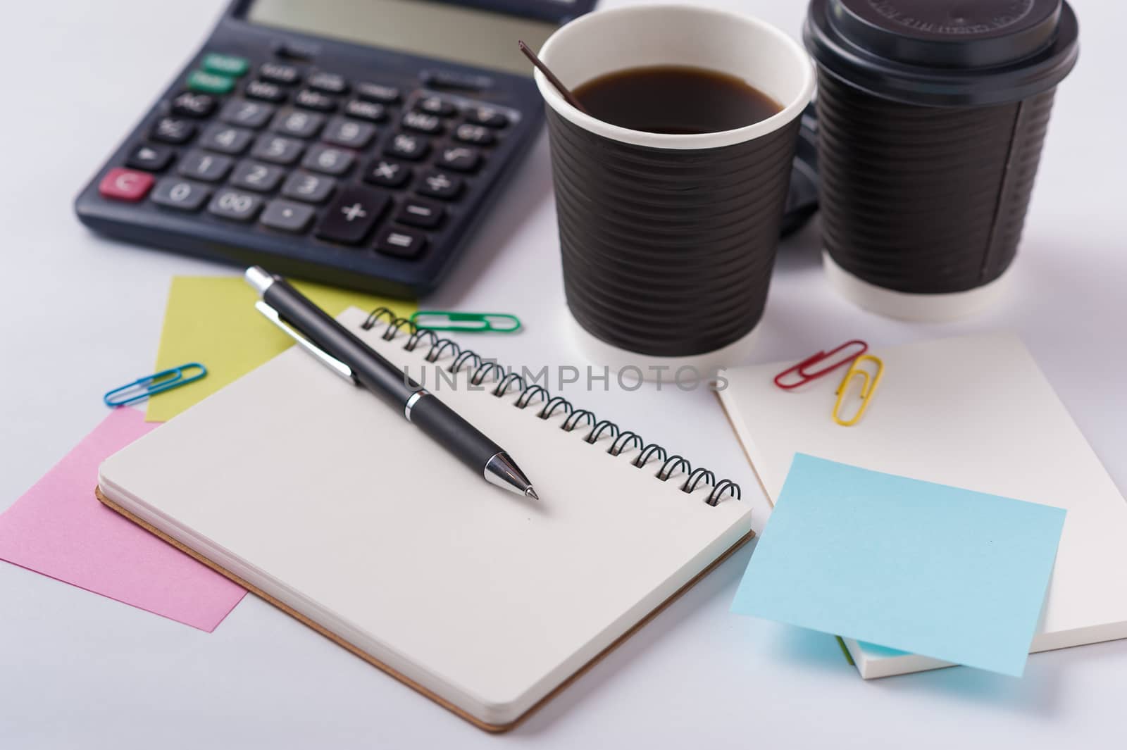 Opened notebook, pen, sticky paper, and take away coffee cup on office table