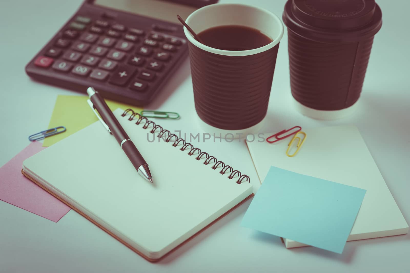 Opened notebook, pen, sticky paper, and take away coffee cup on office table with vintage filter effect