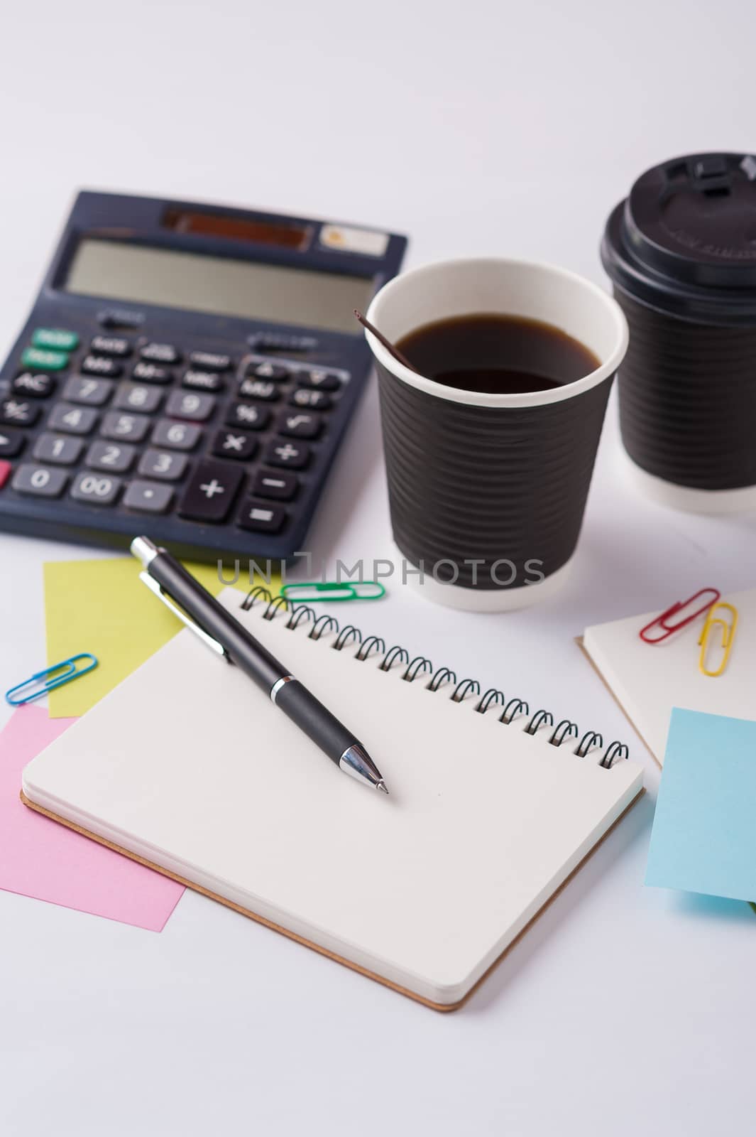 Opened notebook, pen, sticky paper, and take away coffee cup on office table