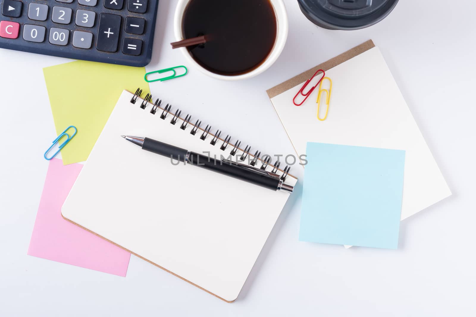 Opened notebook with blank space for text or message, sticky paper, calculator, and take away coffee cup on office table