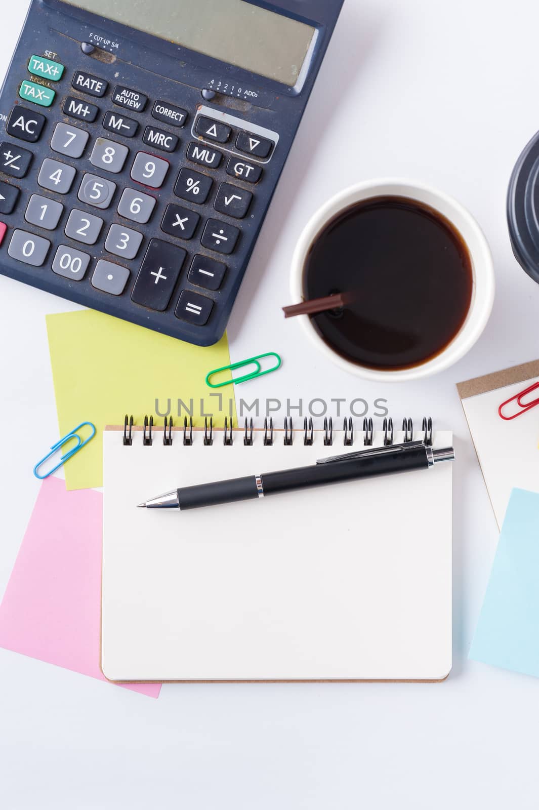 Opened notebook with blank space for text or message, sticky paper, calculator, and take away coffee cup on office table